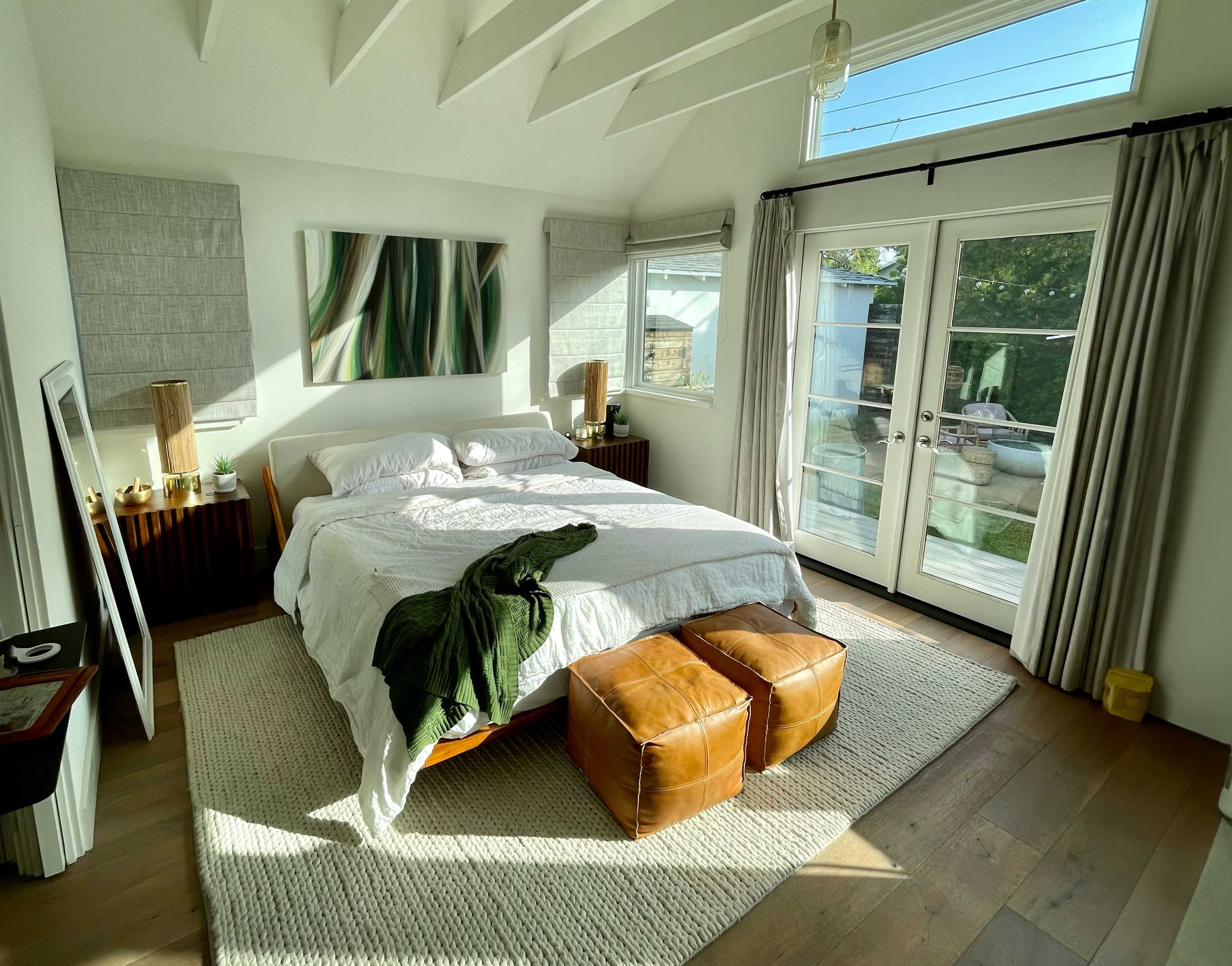 A bright bedroom features a king-sized bed with a white comforter, wooden nightstands, and sliding glass doors that lead to an outdoor patio.