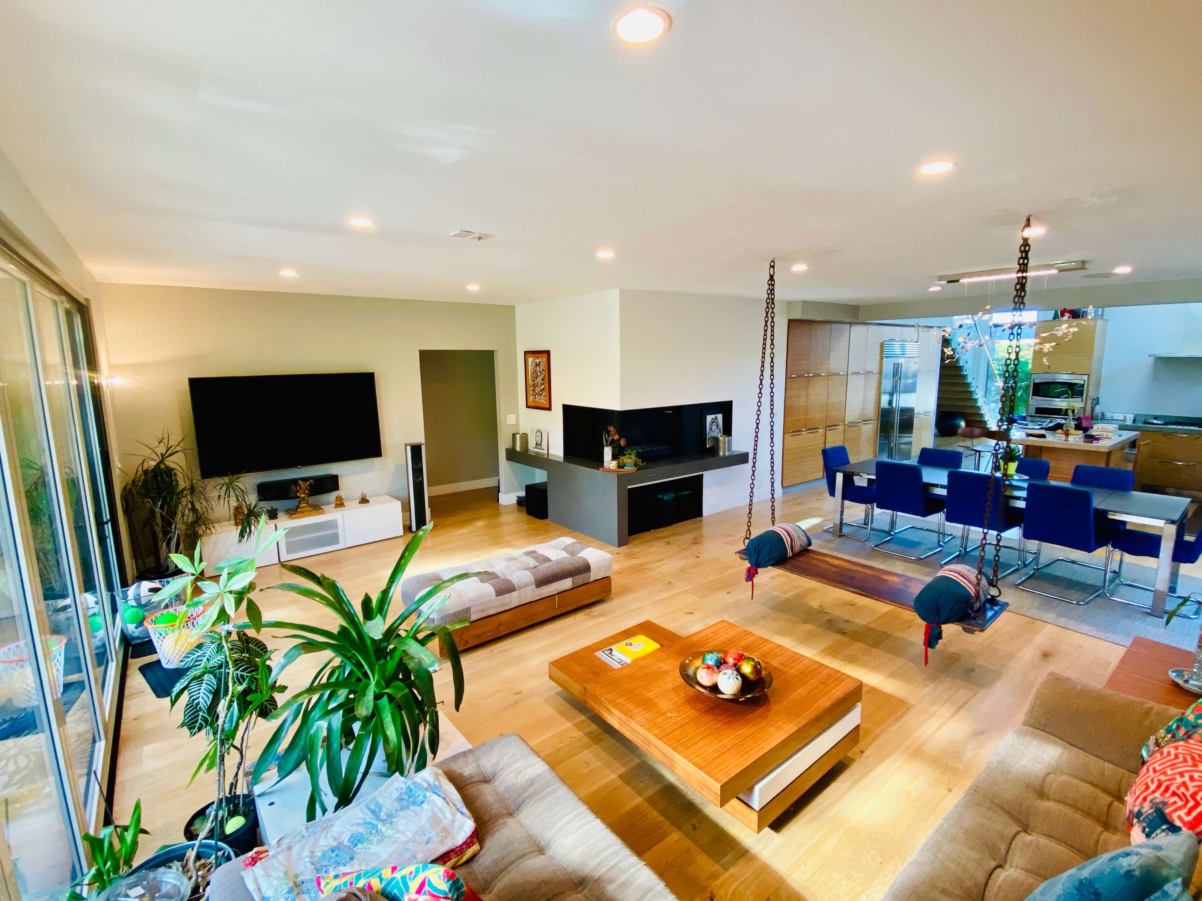 A modern open-concept living area with a television, seating arrangements, a dining table, and a kitchen visible in the background.