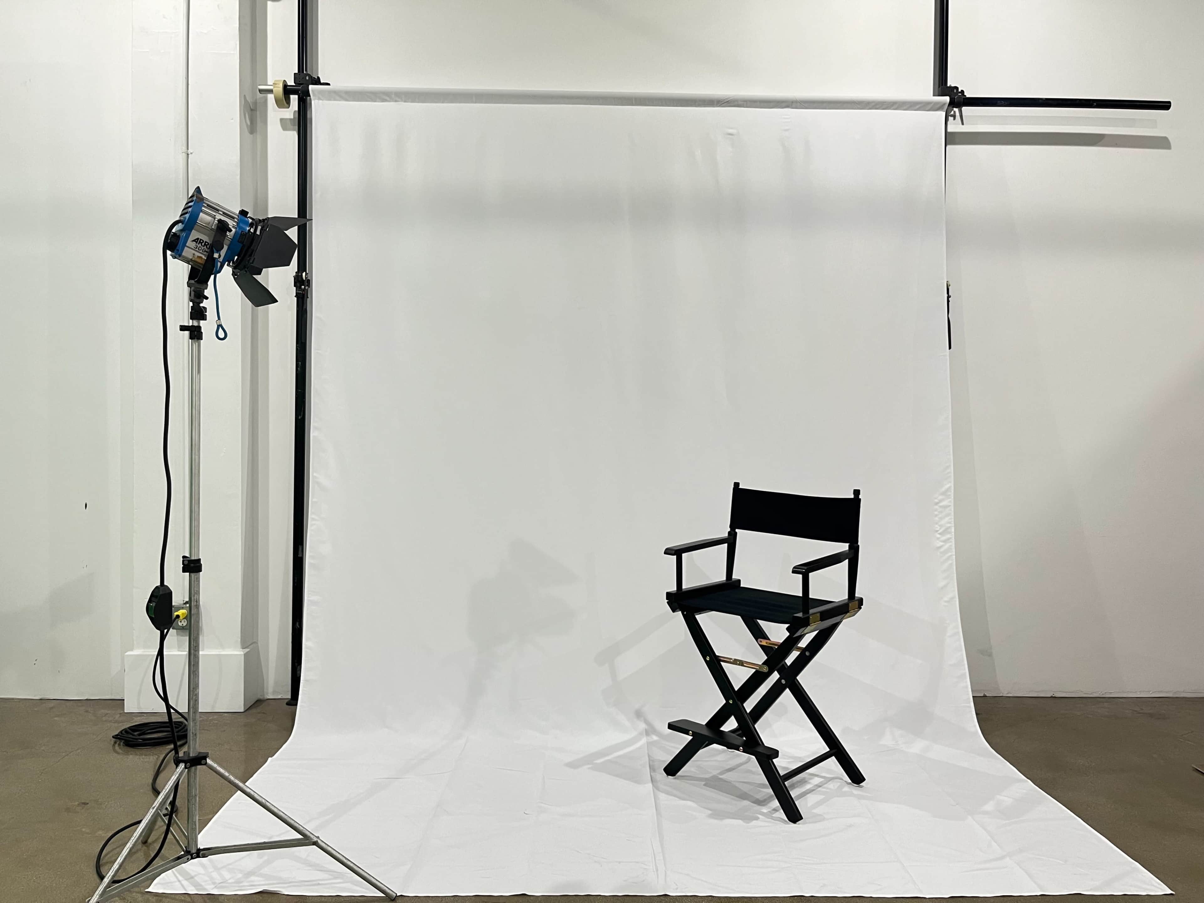 The image features a photography setup with a director's chair placed on a white backdrop and a spotlight positioned nearby.