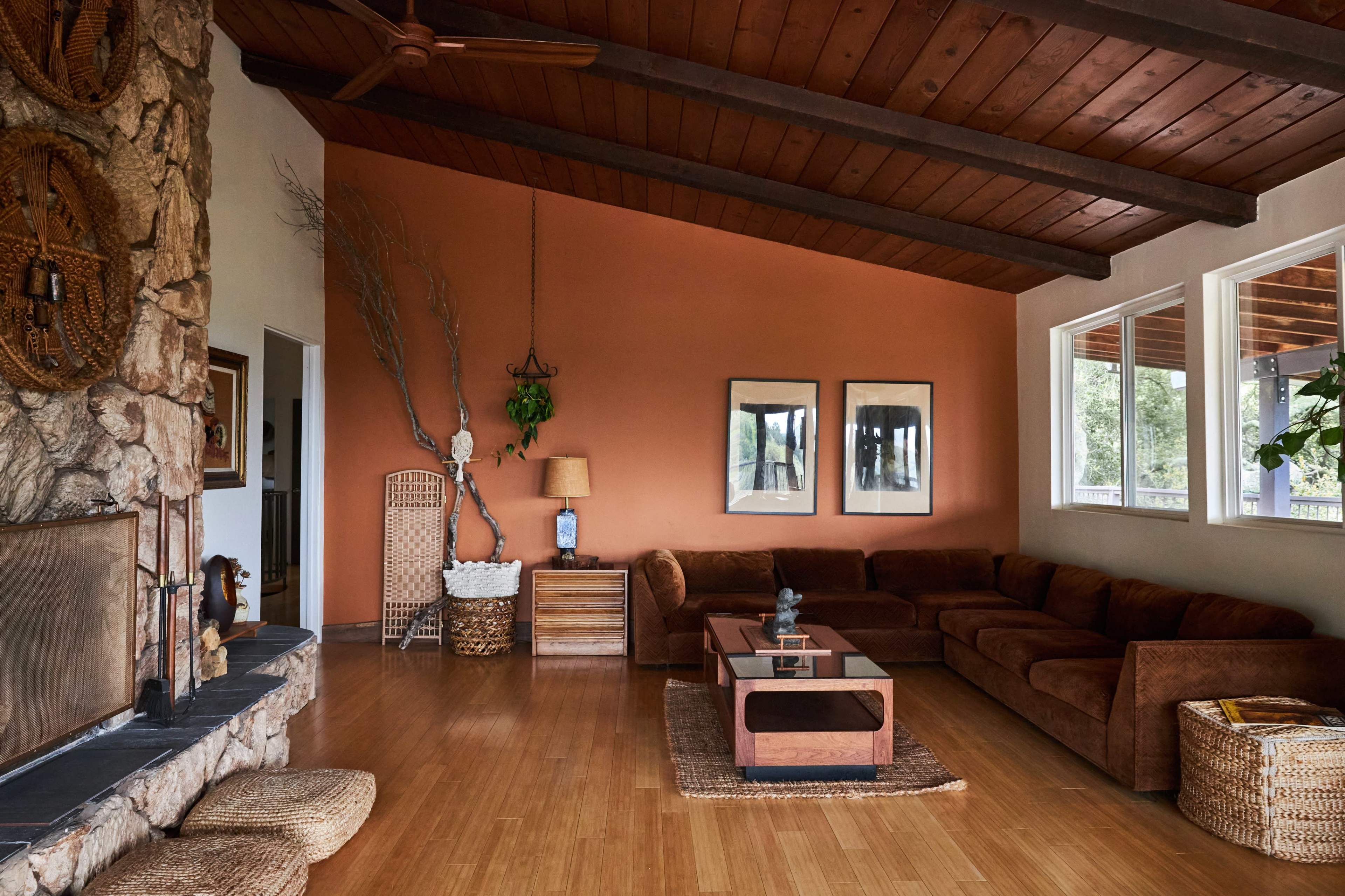 A living room features a brown sectional sofa, wooden coffee table, stone fireplace, and large windows with natural light.