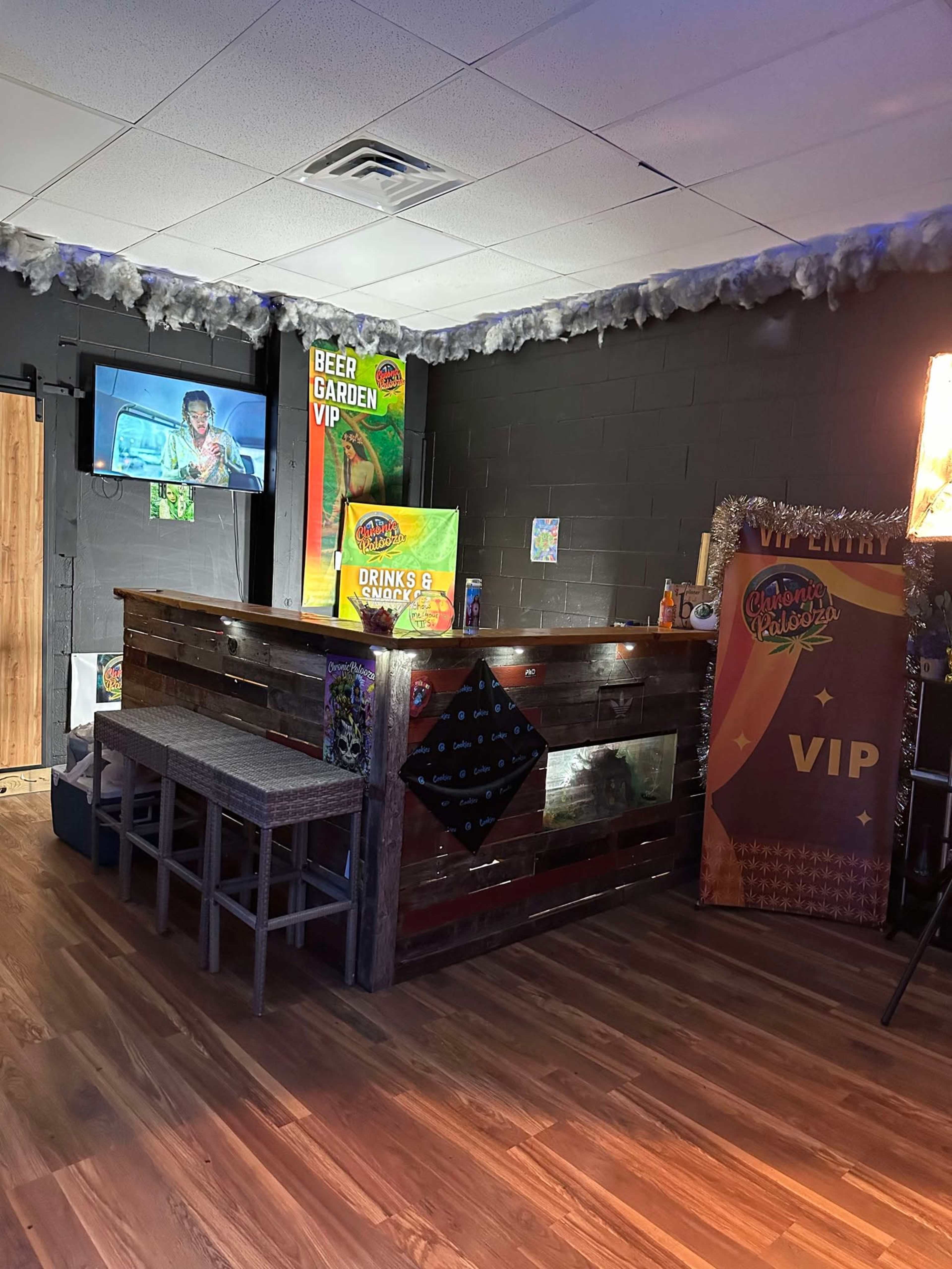 The image shows an interior bar area with a wooden counter, stools, a TV screen on the wall, and promotional signage for drinks and a VIP section.