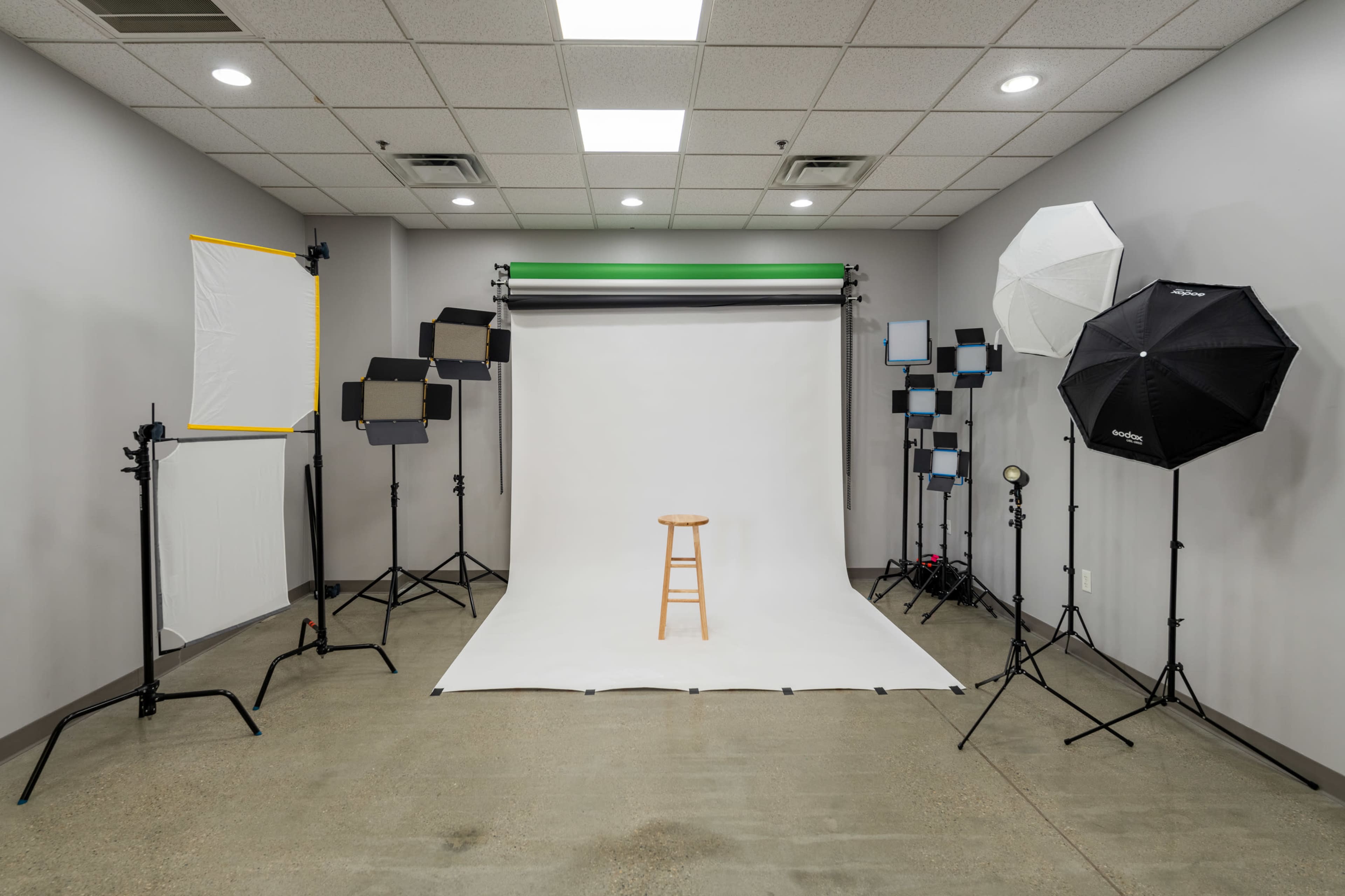 A photography studio is set up with a stool at the center, surrounded by various lighting equipment and backdrops.