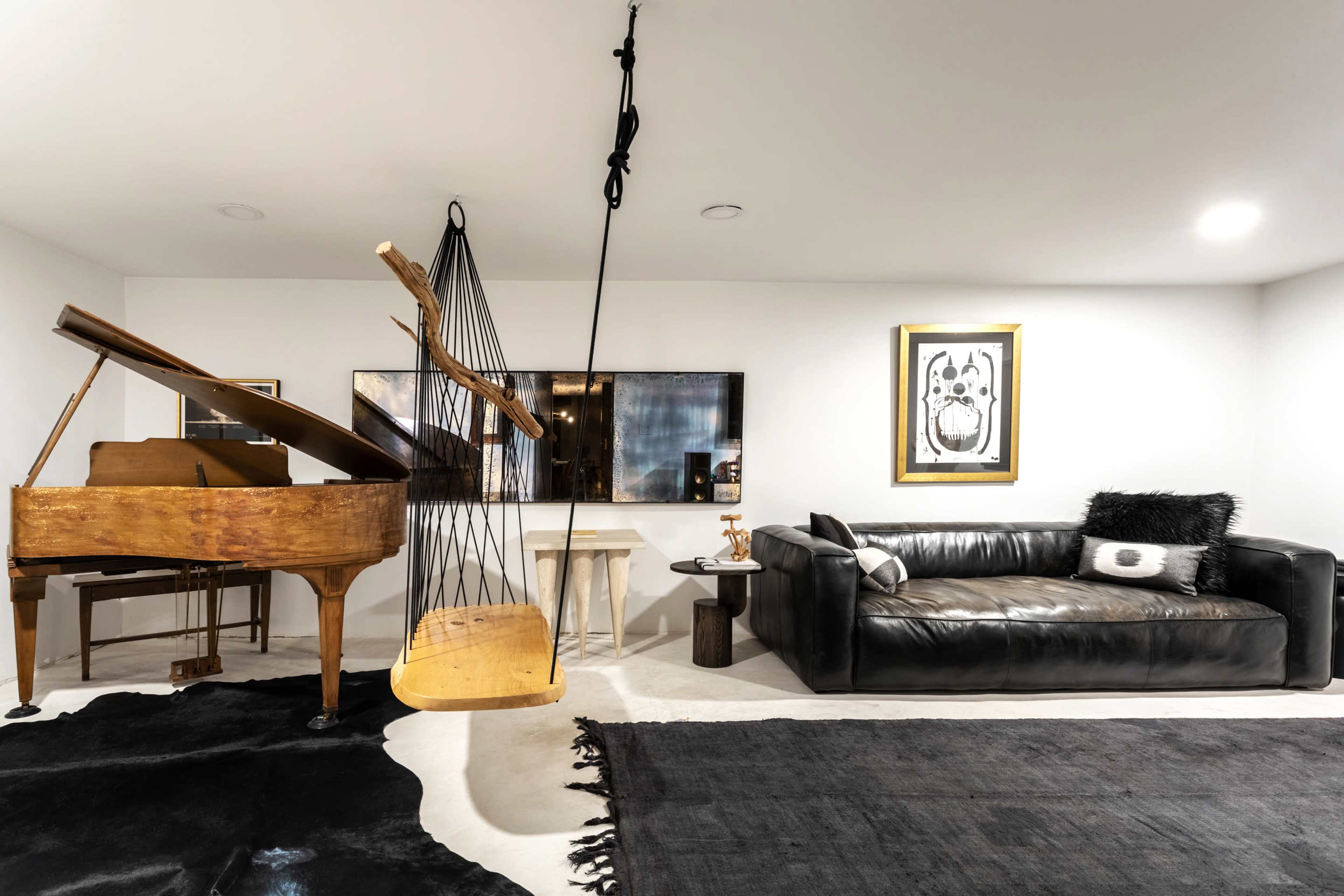 The image shows a modern living space featuring a grand piano, a black leather sofa, a wall-mounted artwork, and a unique hanging sculpture.