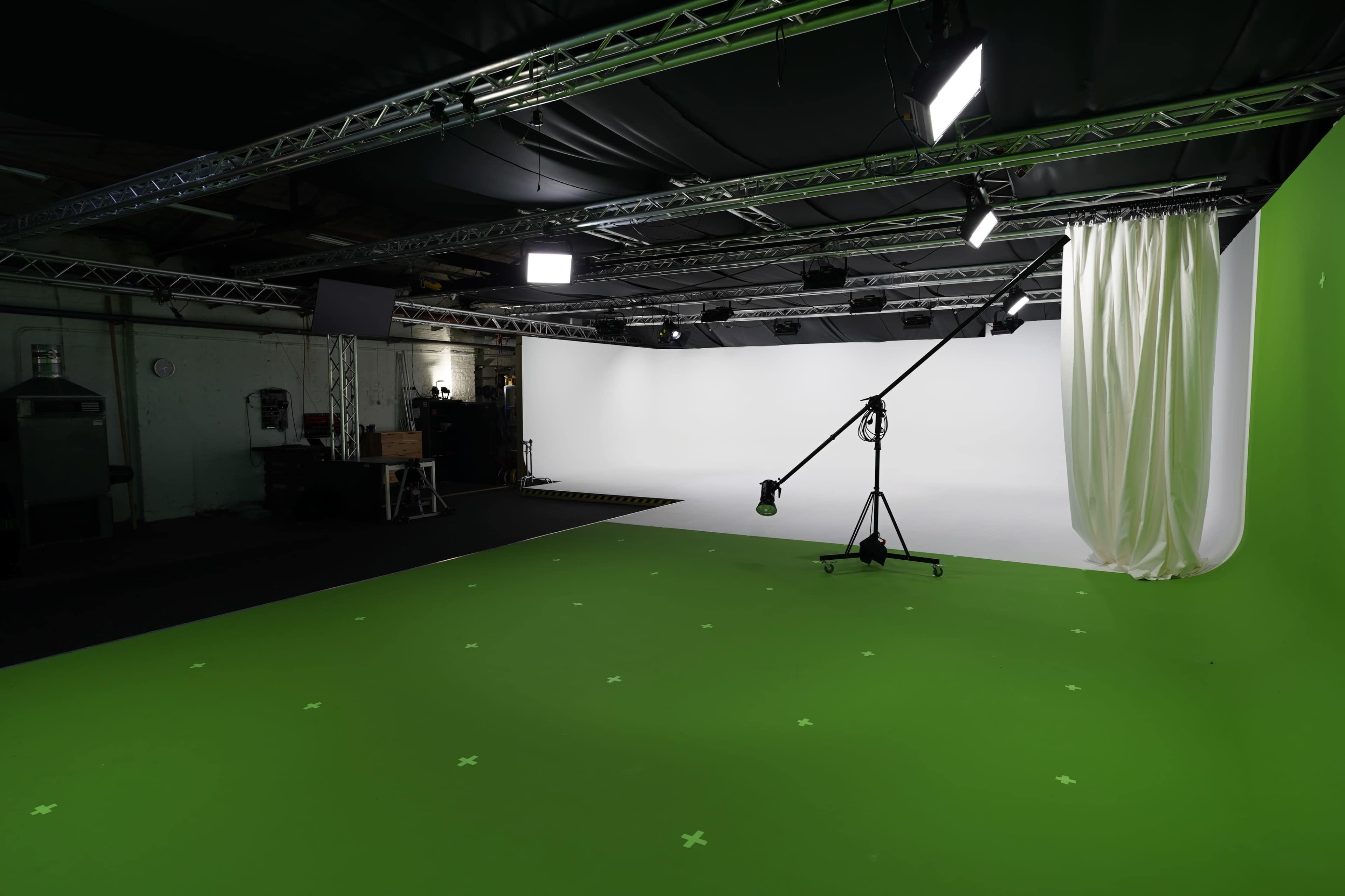 The image shows a studio setup featuring a green screen background, lighting fixtures, and a camera stand on a green floor.