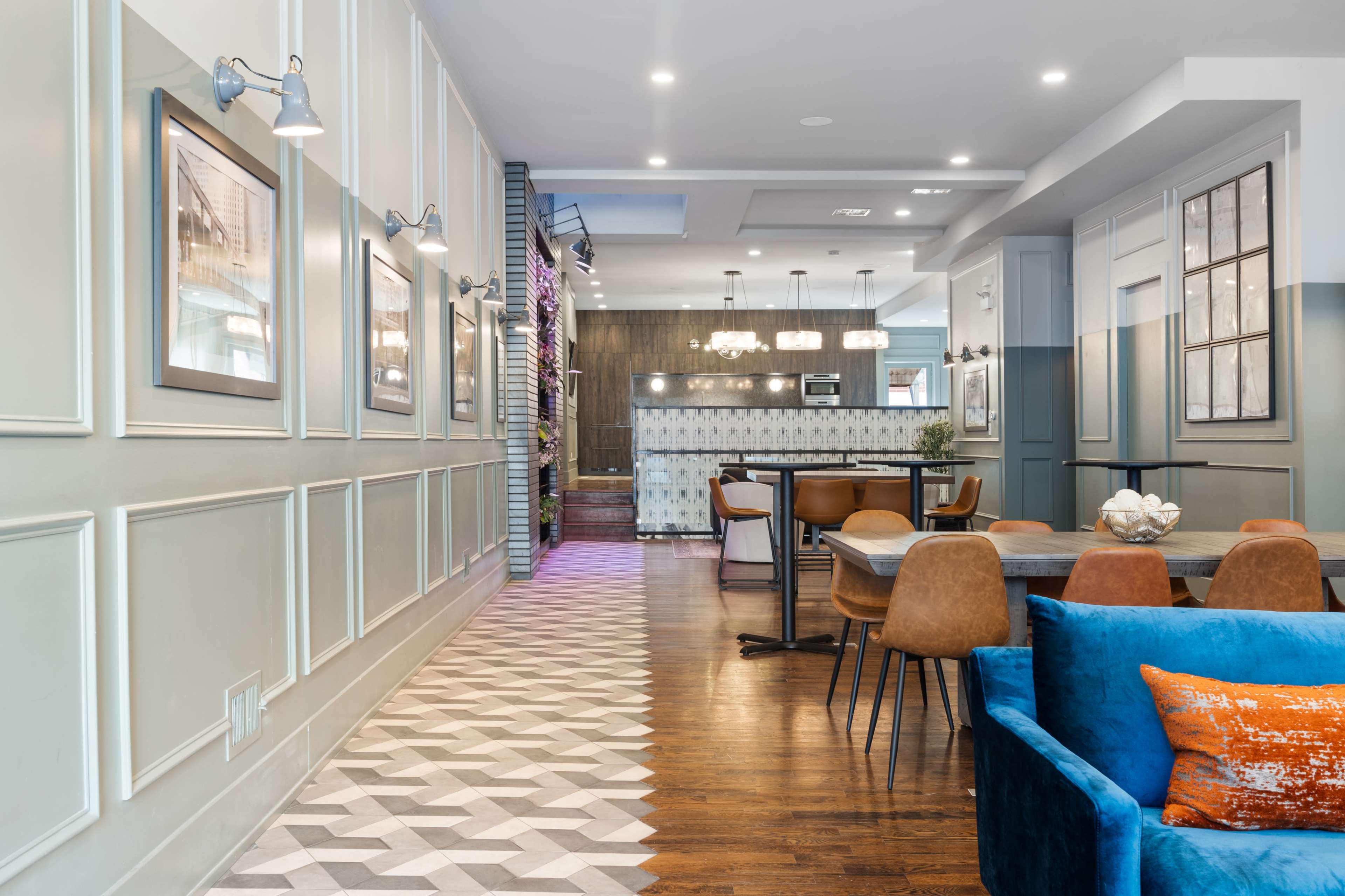 A modern interior space with a patterned tiled floor, a dining area with brown chairs and wooden tables, and walls adorned with framed pictures.