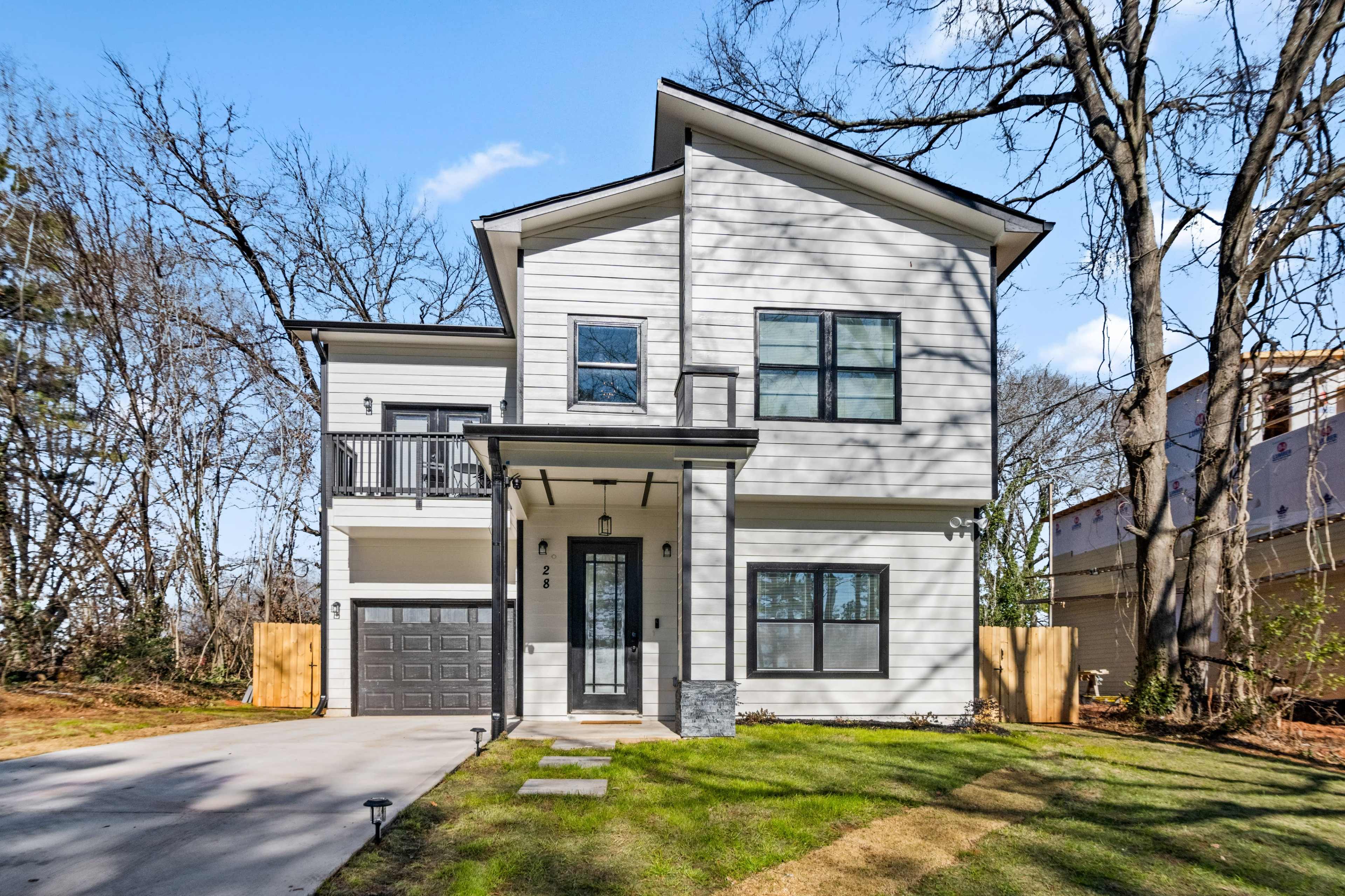 The image shows a modern two-story house with a gray exterior, a front porch, and a paved driveway surrounded by a lawn.