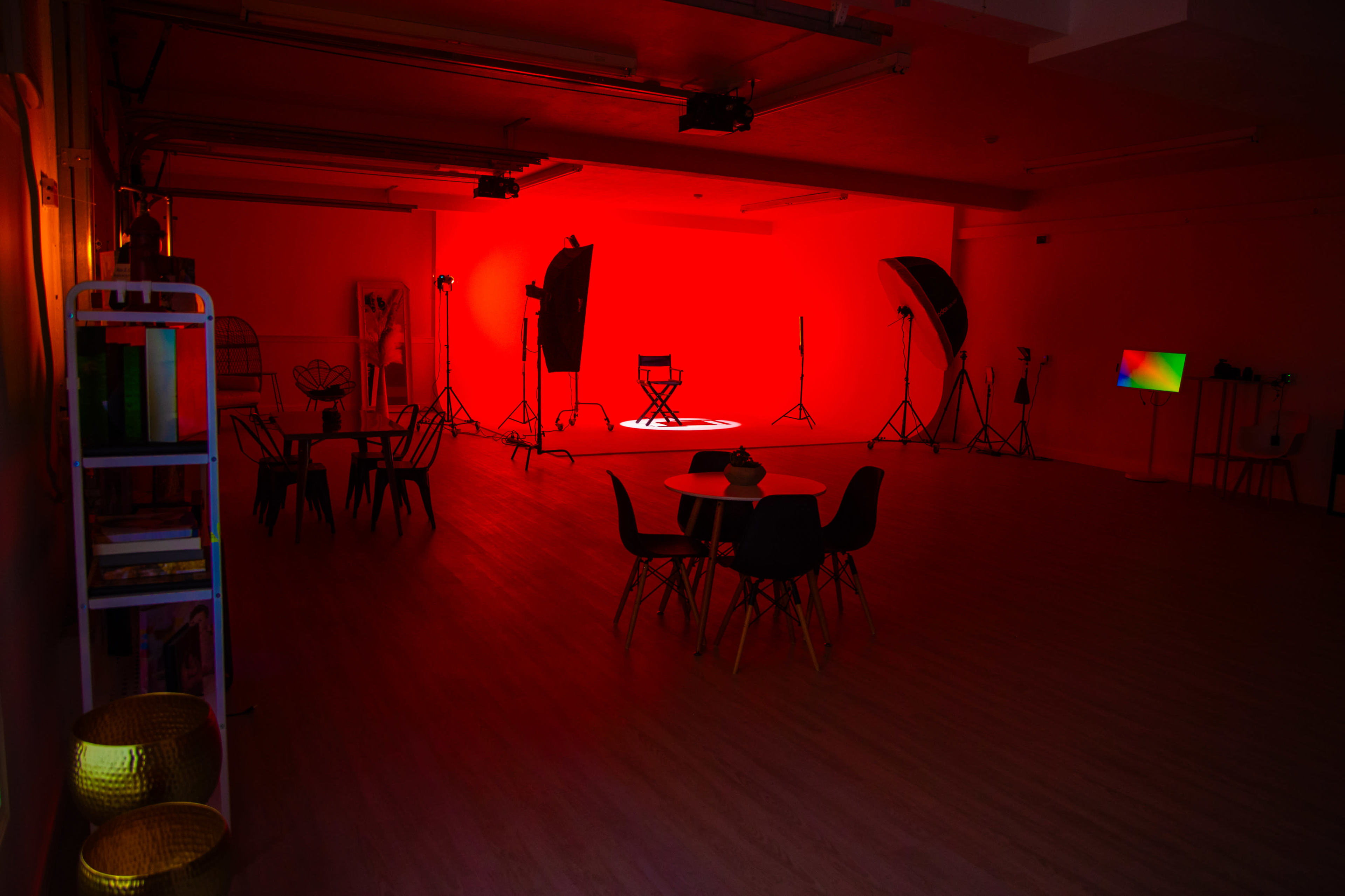 The image shows a spacious studio with red lighting, featuring various photography equipment and empty furniture arrangements.