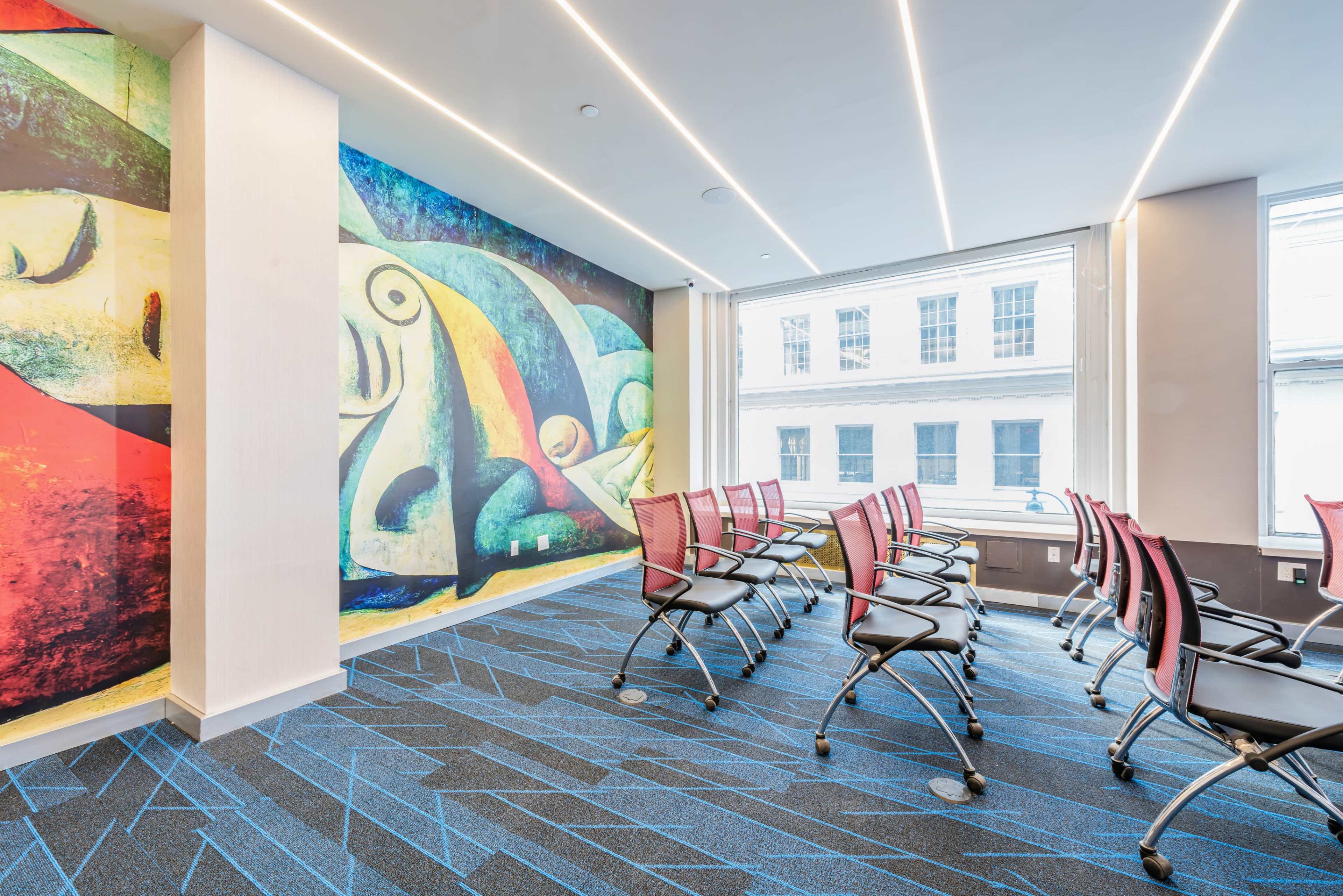The image shows a modern meeting room featuring a colorful mural on one wall and several rows of black chairs arranged for a presentation.