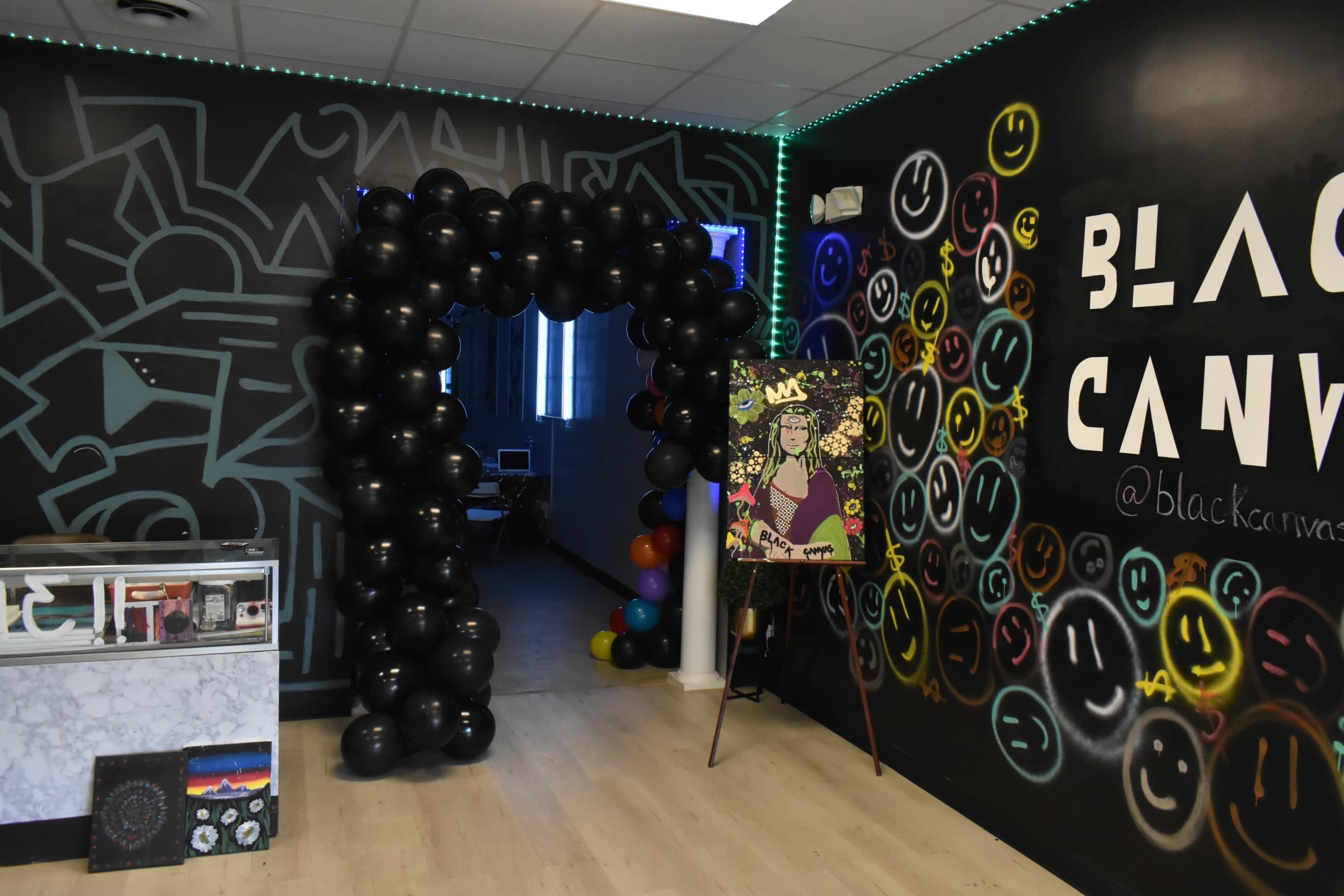 An entrance adorned with black balloons leading into a room with colorful graffiti and an artwork displayed on an easel.