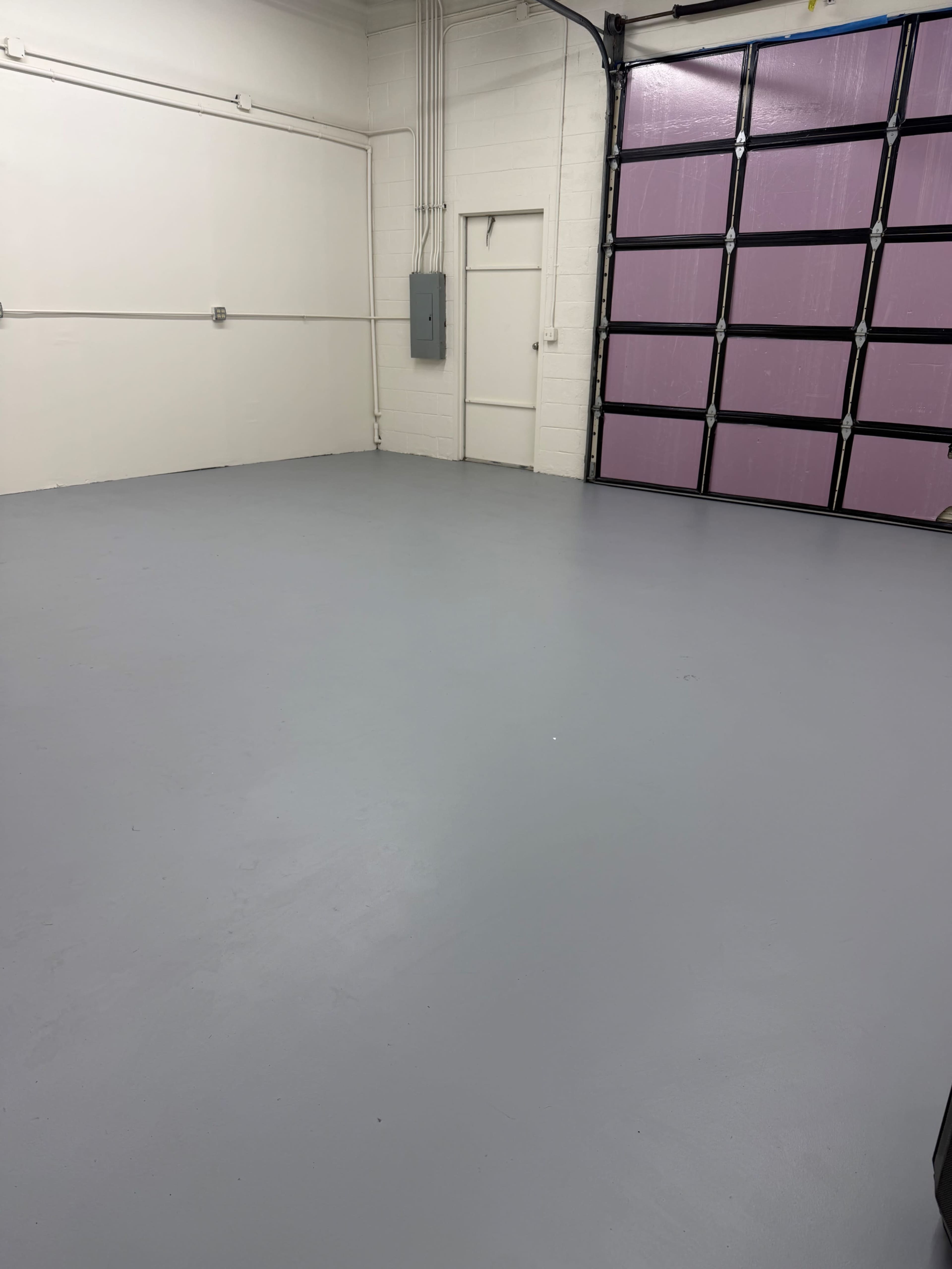 The image shows an empty garage or storage space with a gray concrete floor and a large garage door featuring purple panels.