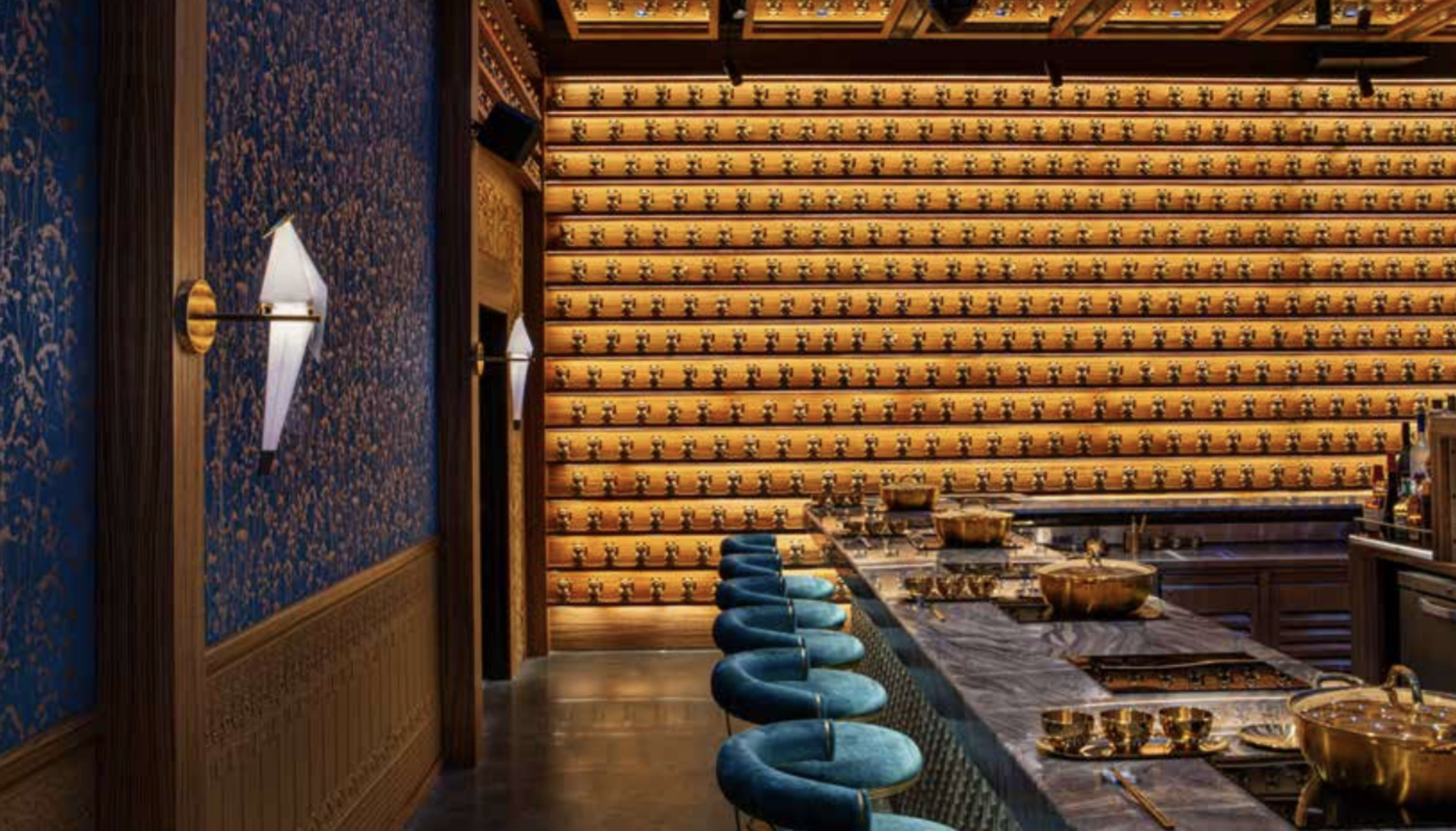 The image shows a stylish restaurant interior with a bar area featuring a long countertop, several cooking pots, and a wall adorned with numerous small decorative items.