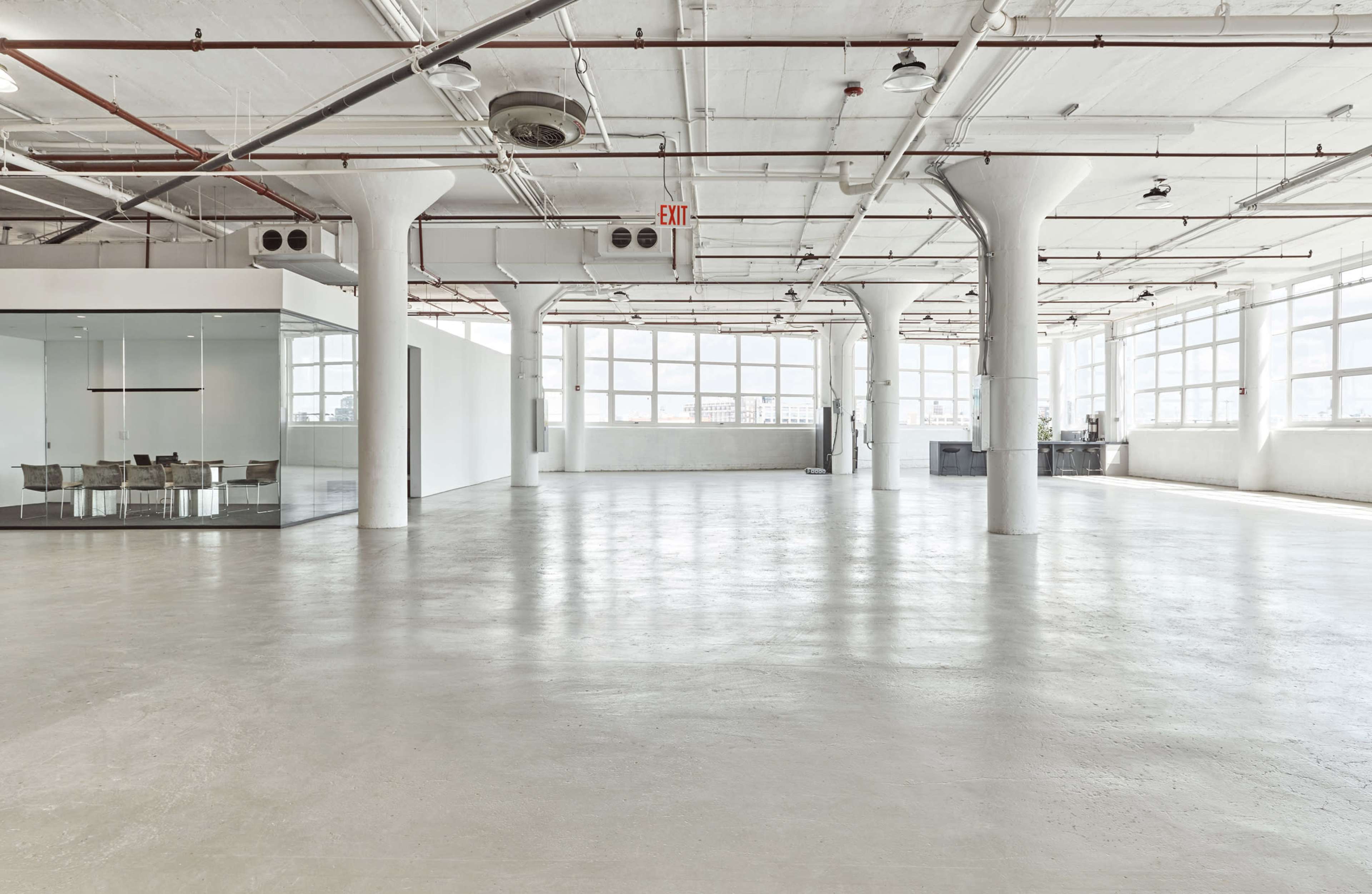 A spacious, empty industrial-style room with large windows and white concrete floors.