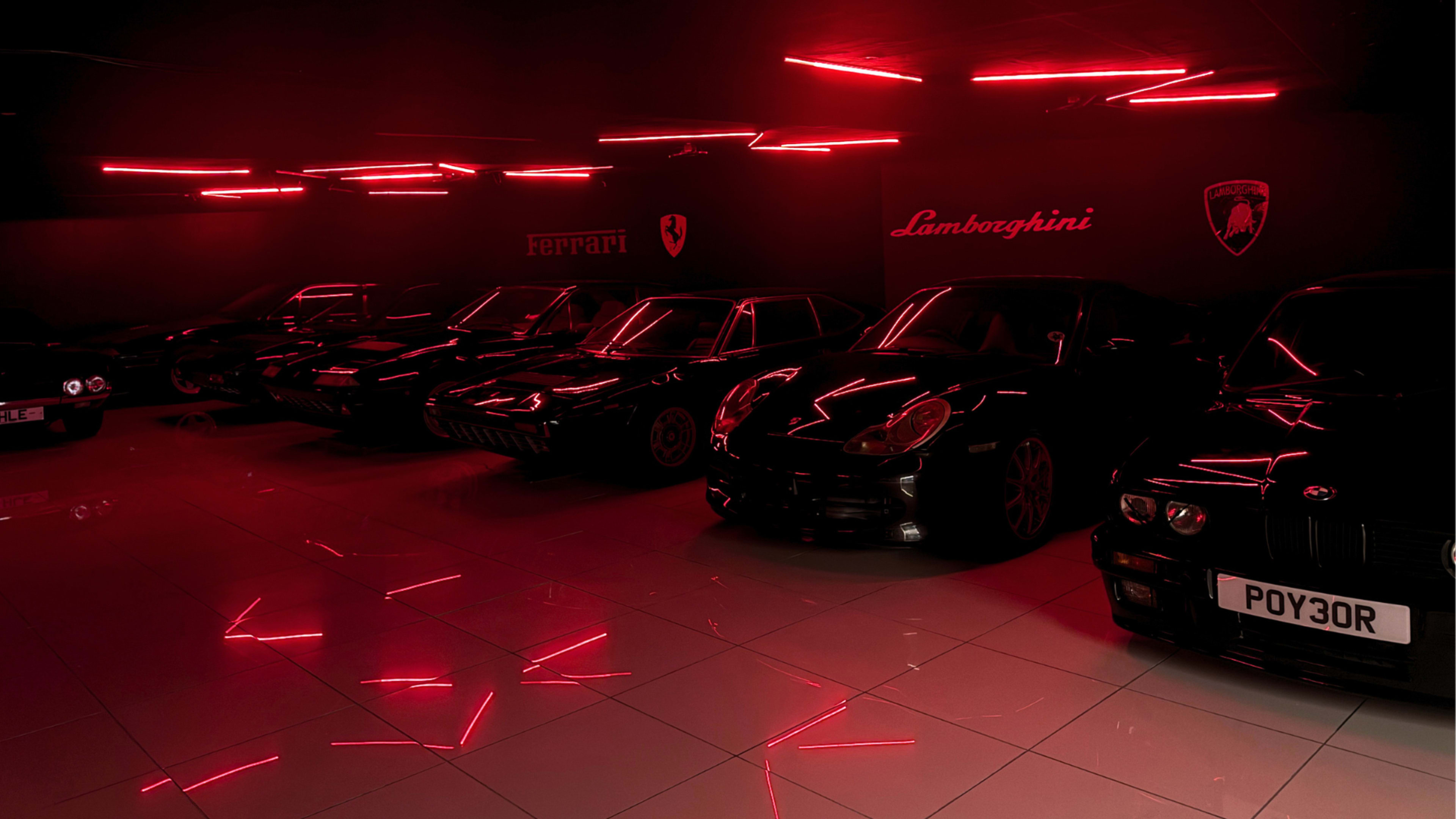 The image features a lineup of black luxury cars illuminated by red neon lights in a dimly lit showroom.