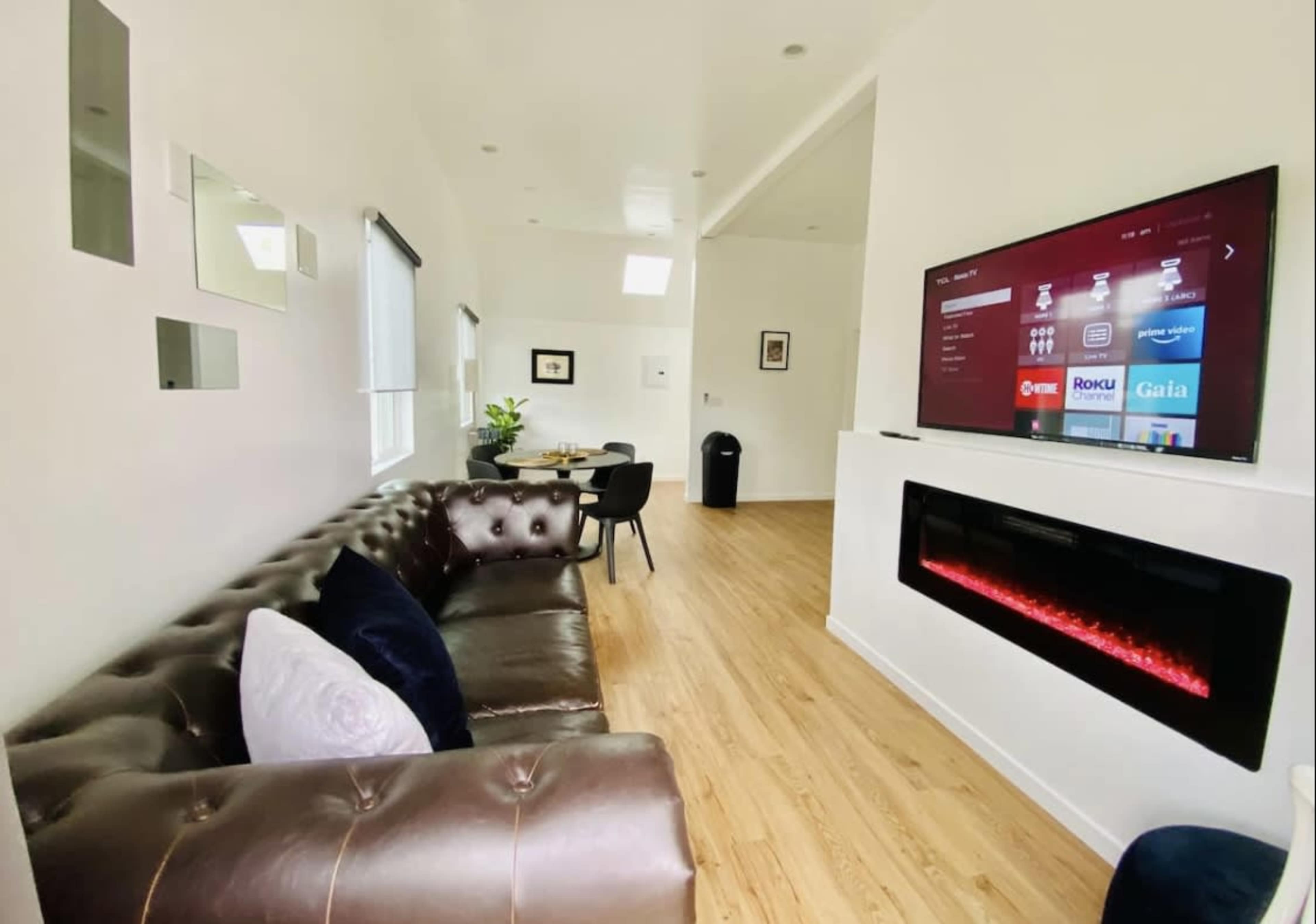 A modern living room featuring a dark leather sofa, a wall-mounted television displaying a menu, and an electric fireplace beneath it.