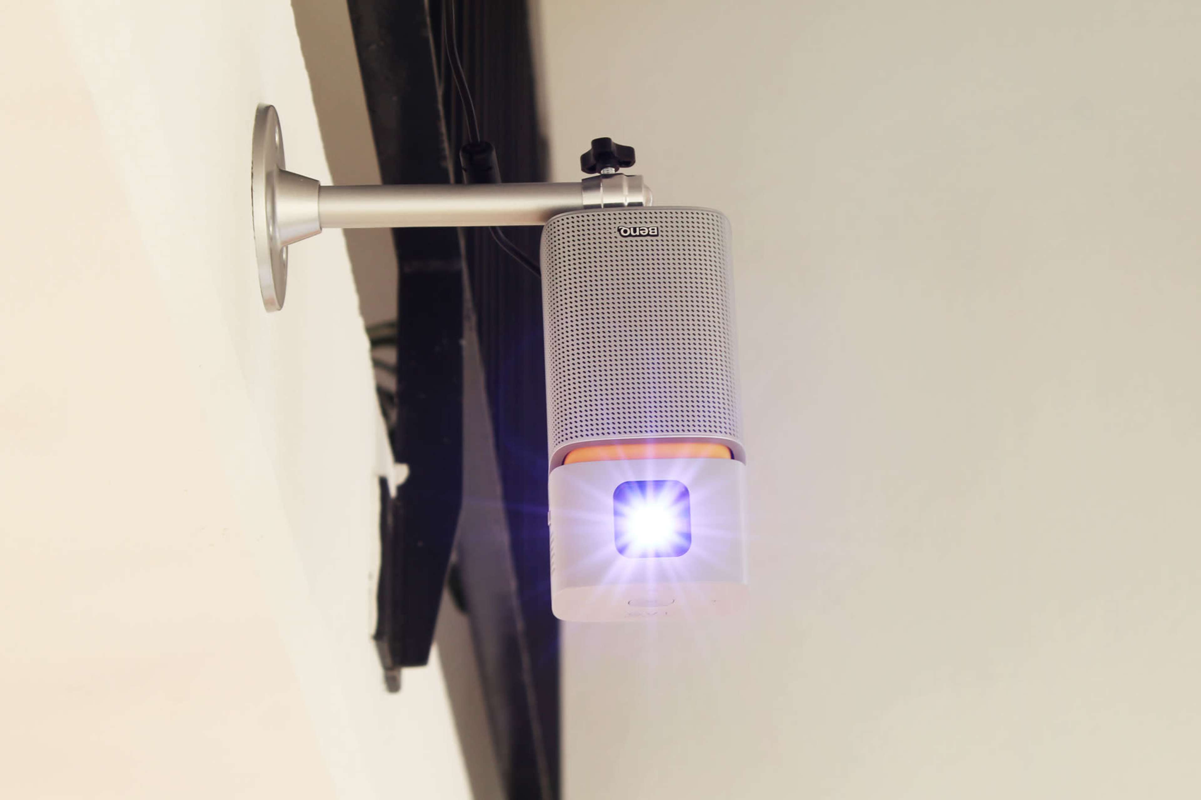 A projector is mounted on a ceiling bracket, projecting light onto a surface below.