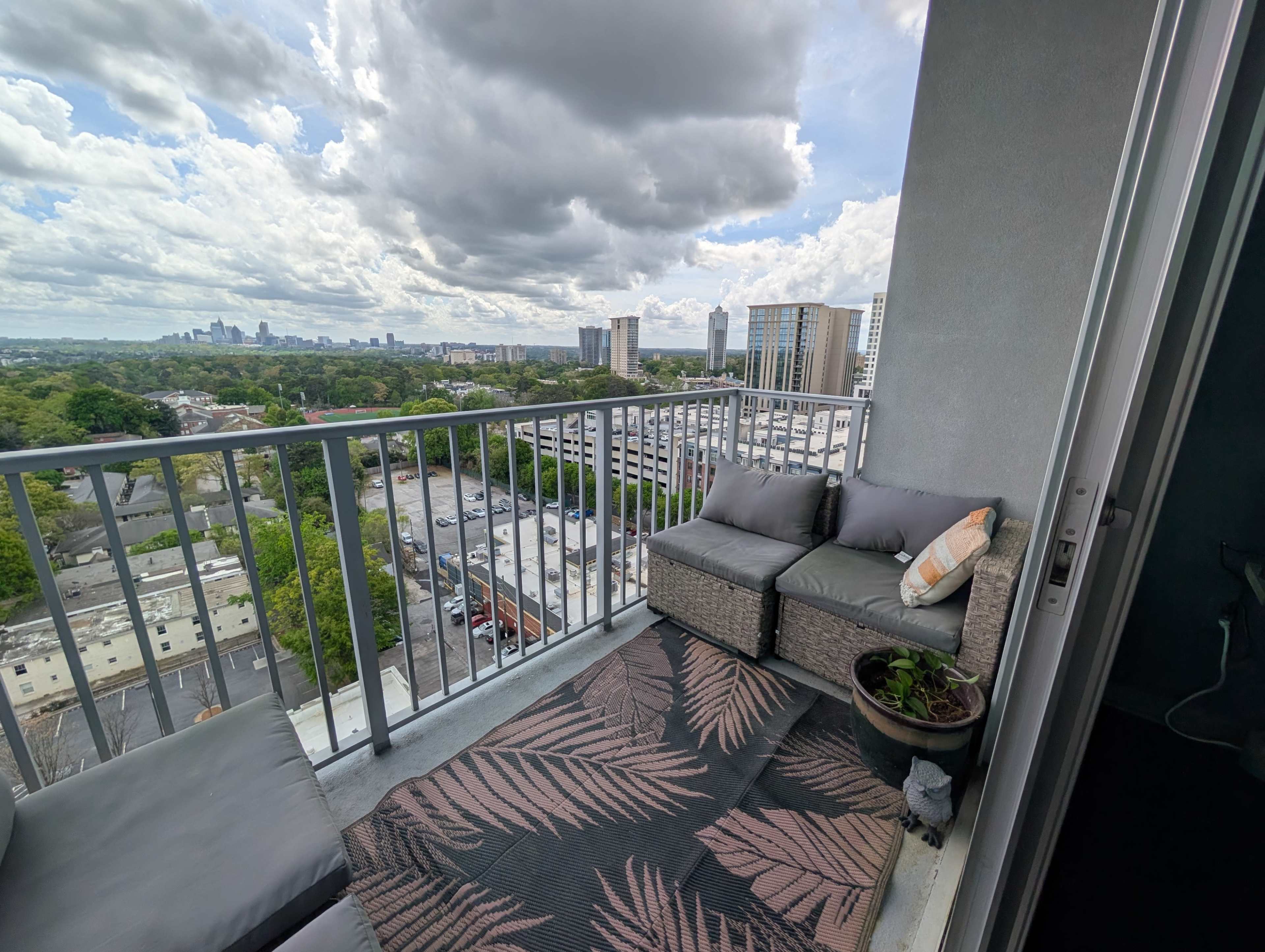 A balcony with a seating area overlooks a cityscape under a cloudy sky.