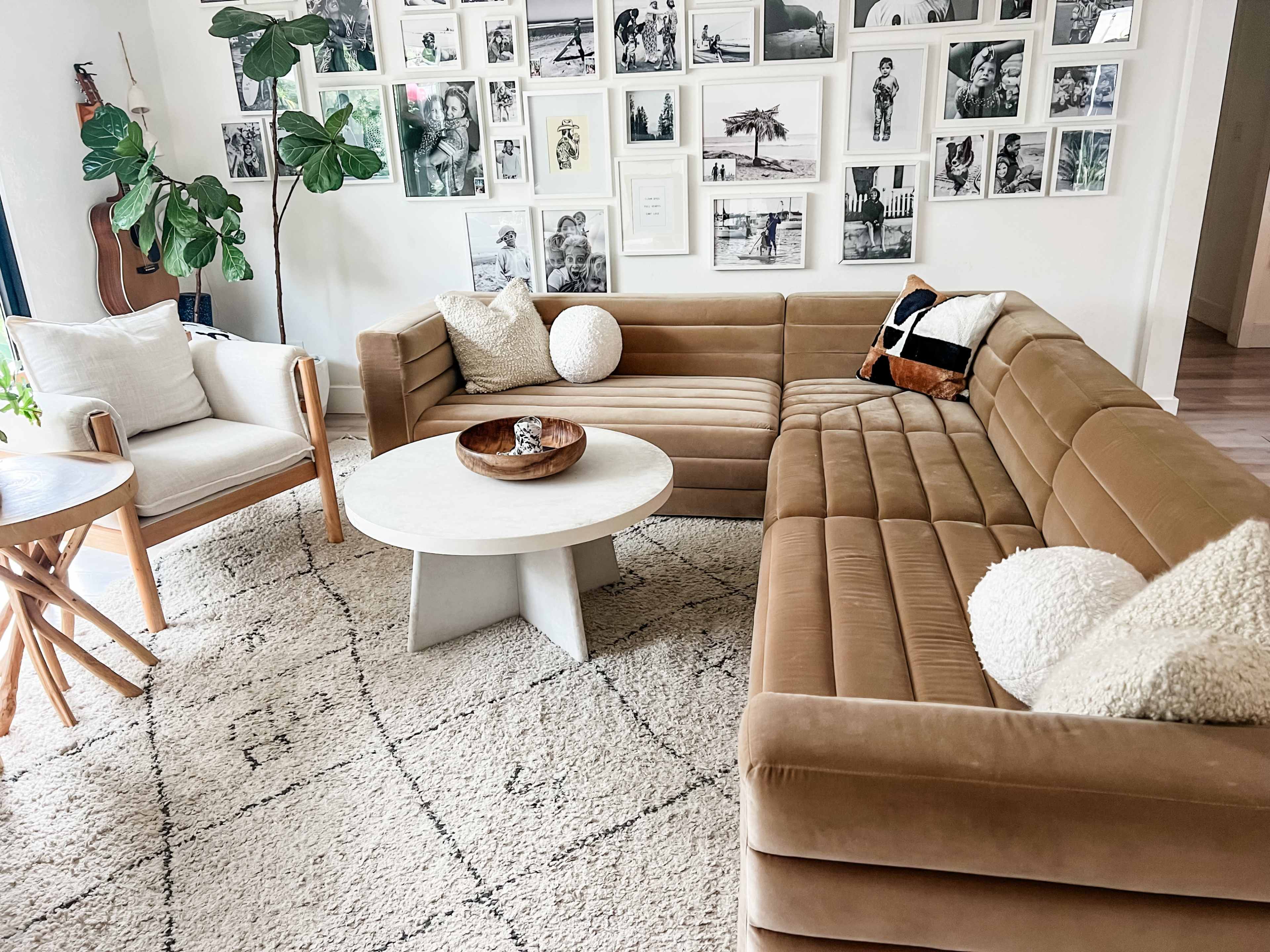 A cozy living room with a tan sectional sofa, a round coffee table, and an assortment of framed black-and-white photographs on the wall.