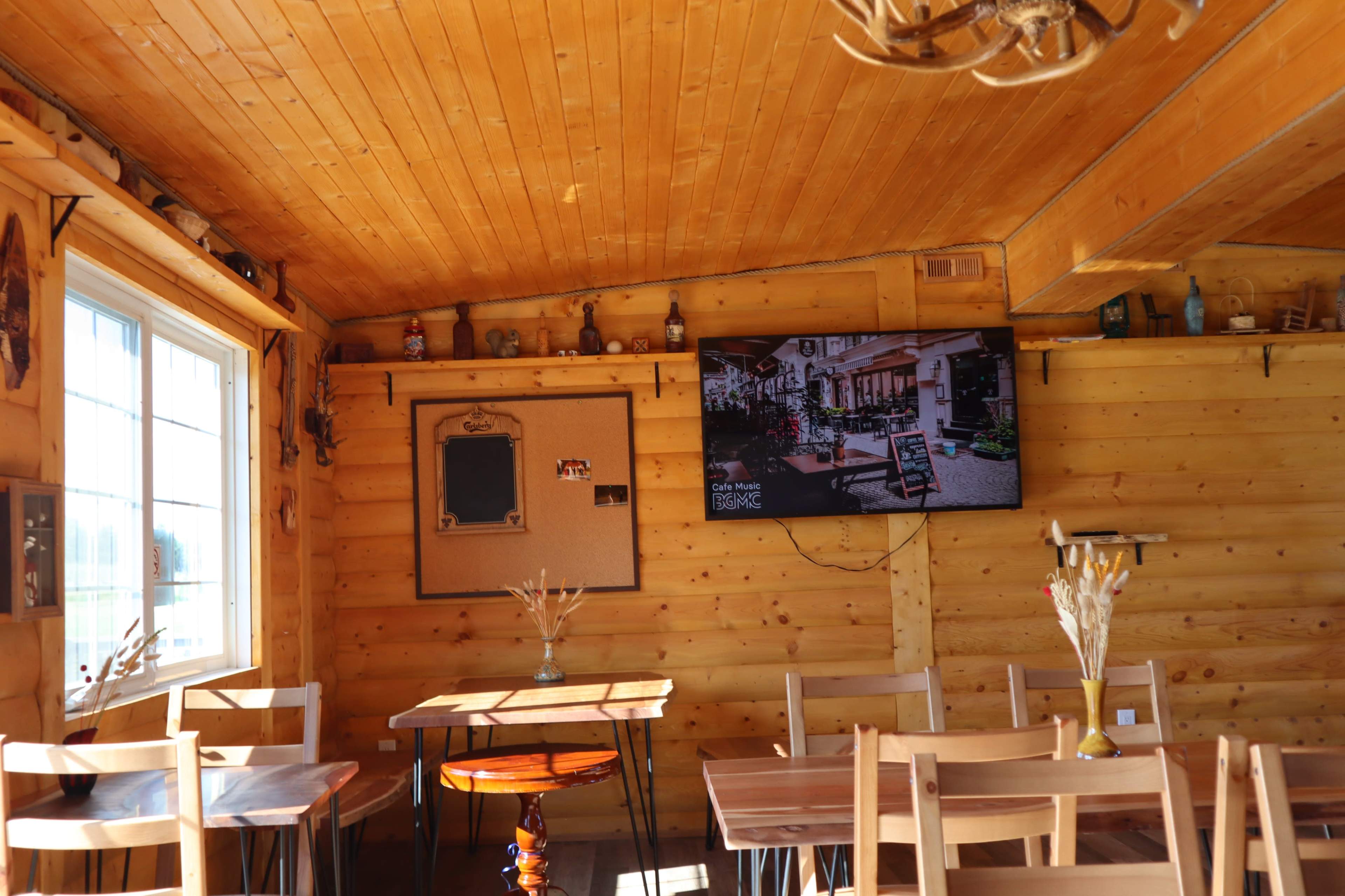 The image shows a wooden interior of a cozy dining area with tables and a large TV mounted on the wall.