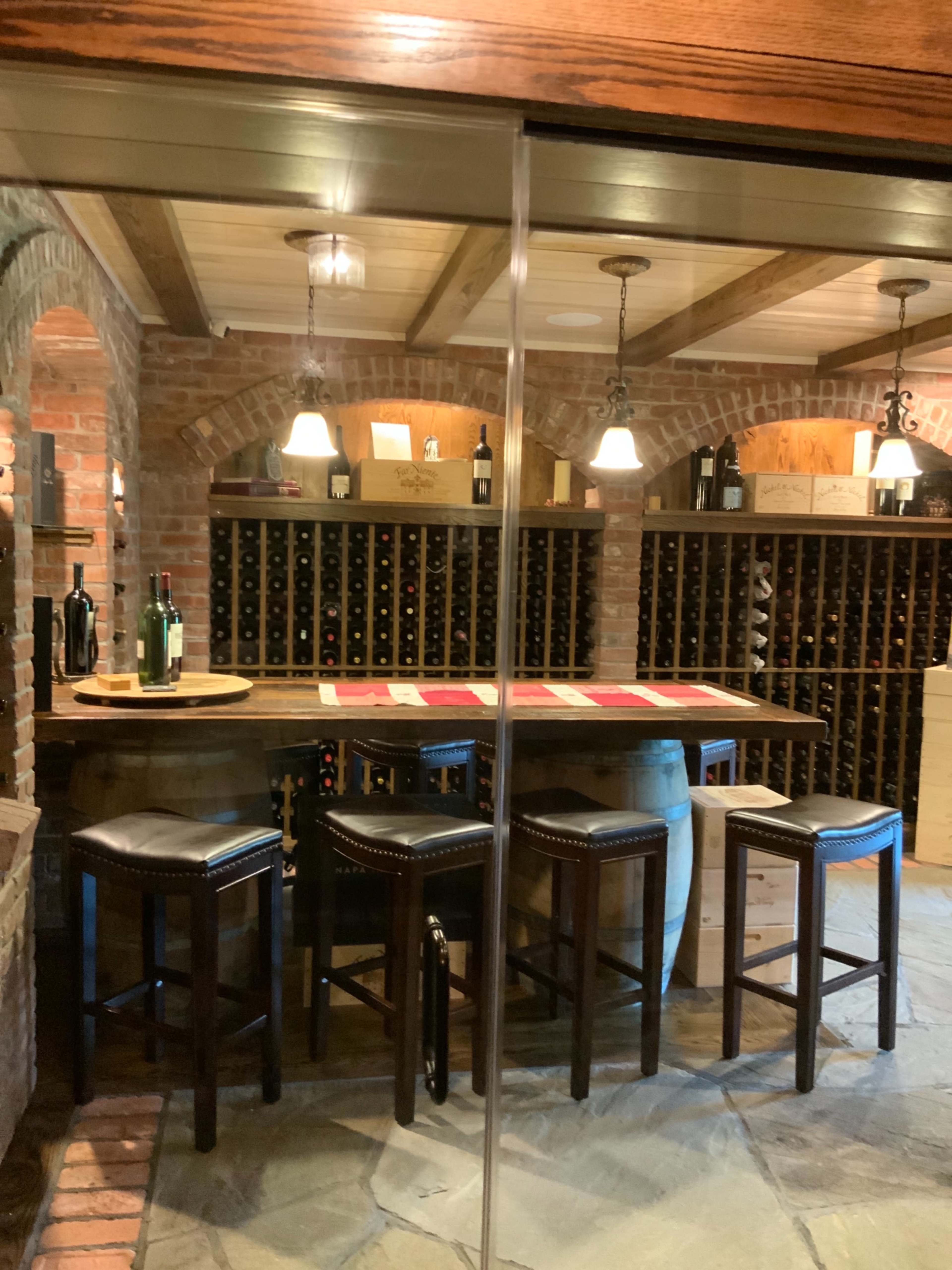 A wine cellar featuring wooden barrels as tables, high-backed stools, and neatly arranged wine bottles on the walls.