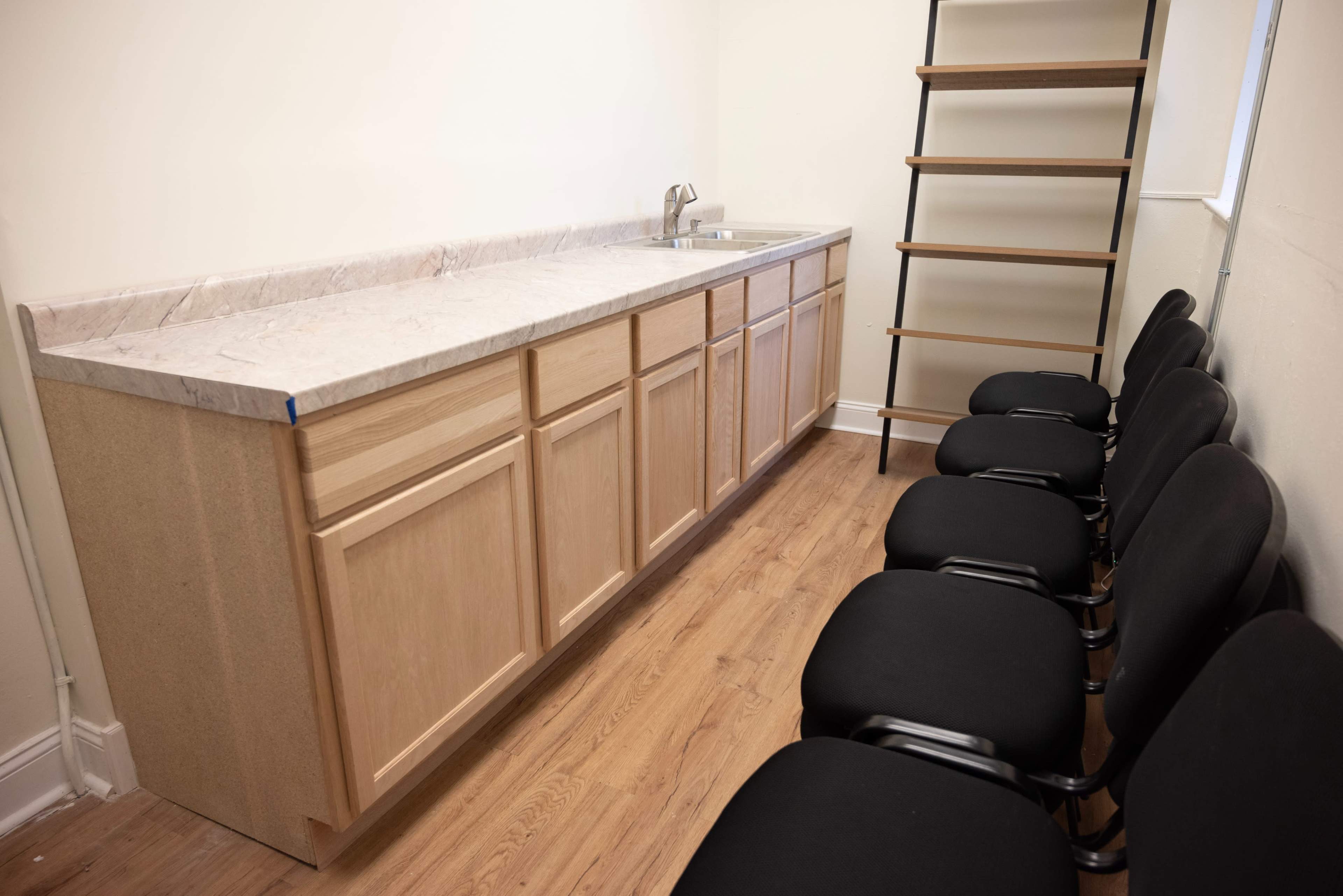 A kitchen area with a long countertop, a sink, and a row of black chairs along one side.