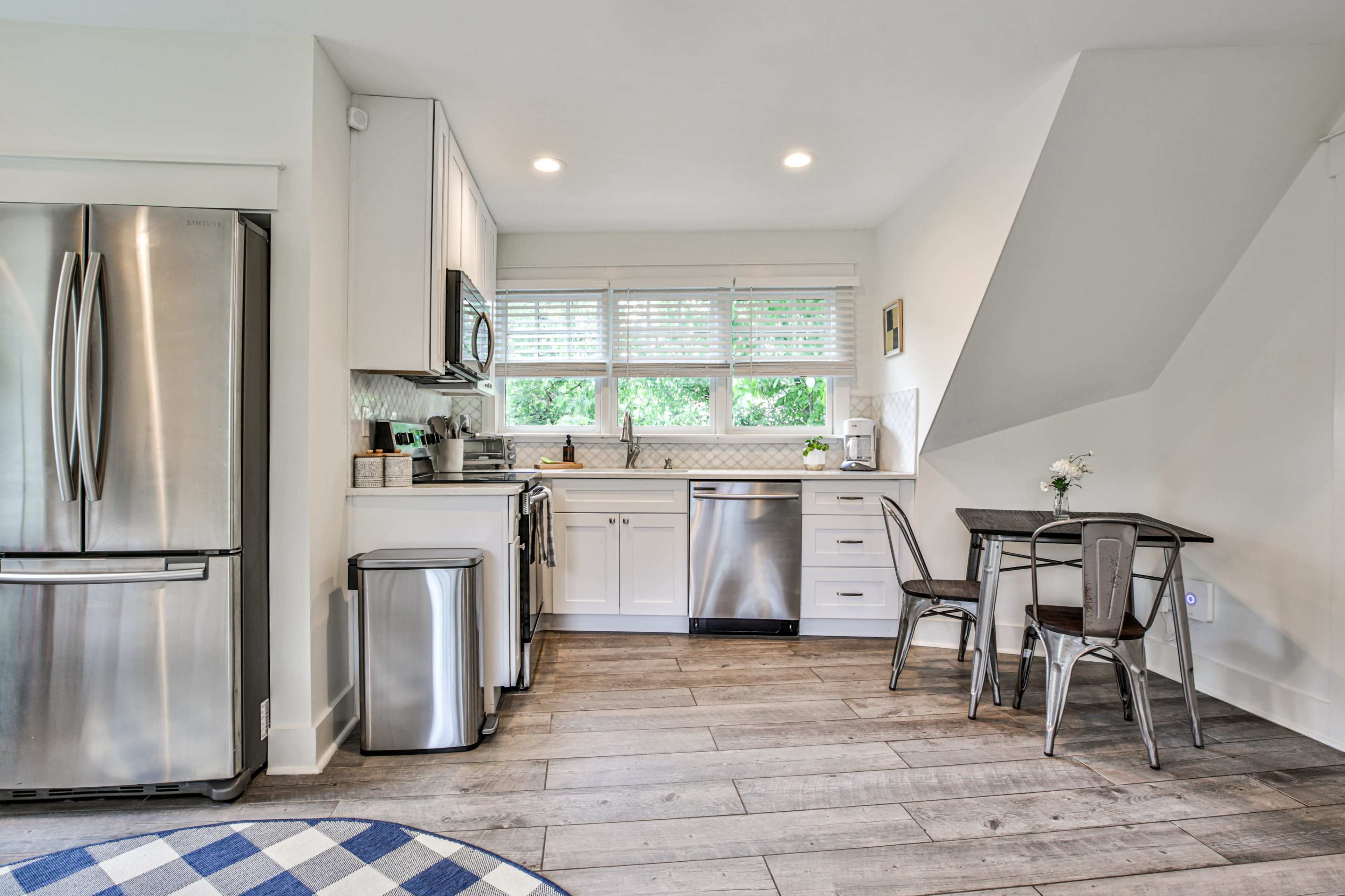 A modern kitchen with stainless steel appliances, white cabinetry, and a small dining table with two chairs.