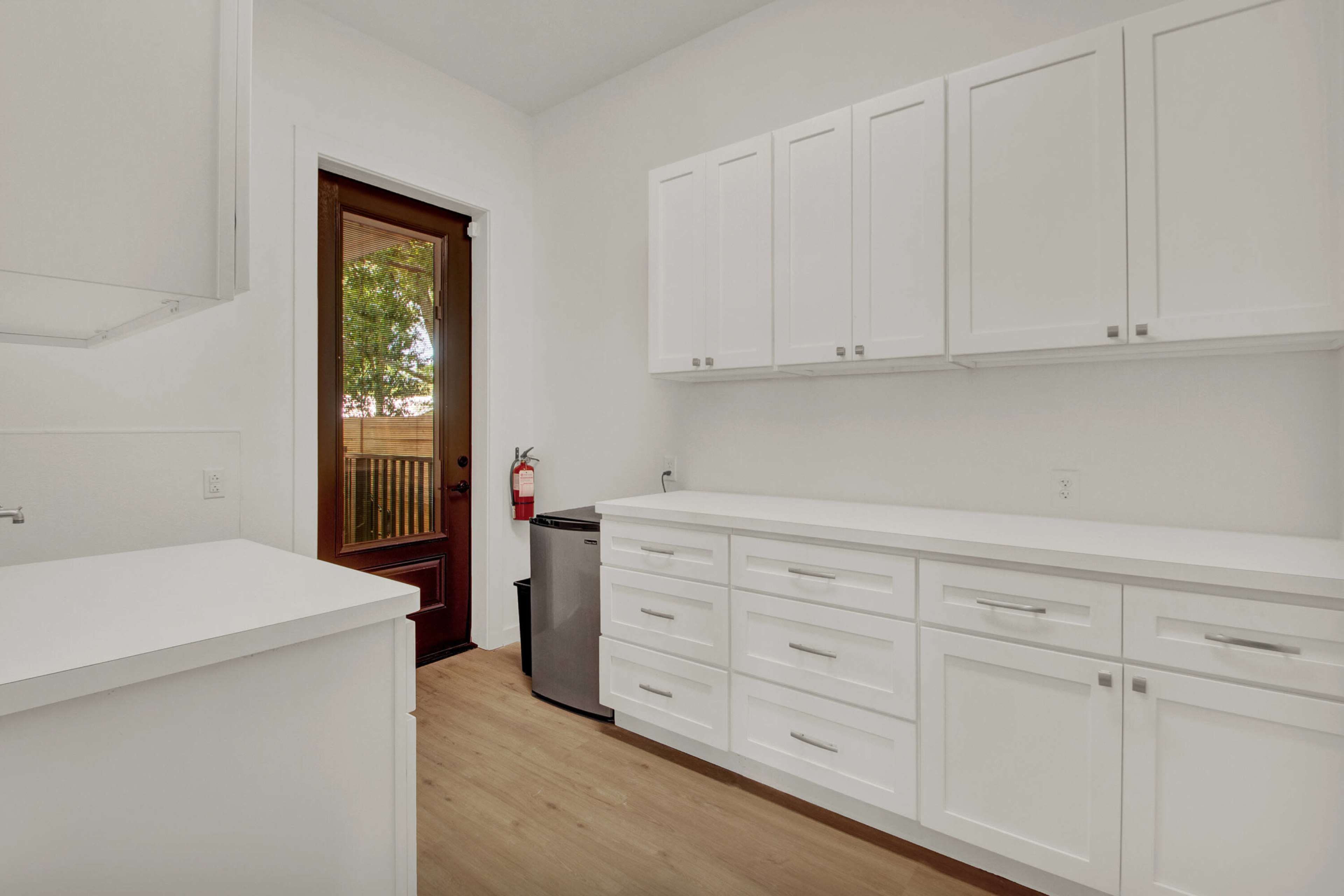 The image shows a modern kitchen with white cabinetry, a countertop, and a door leading outside.