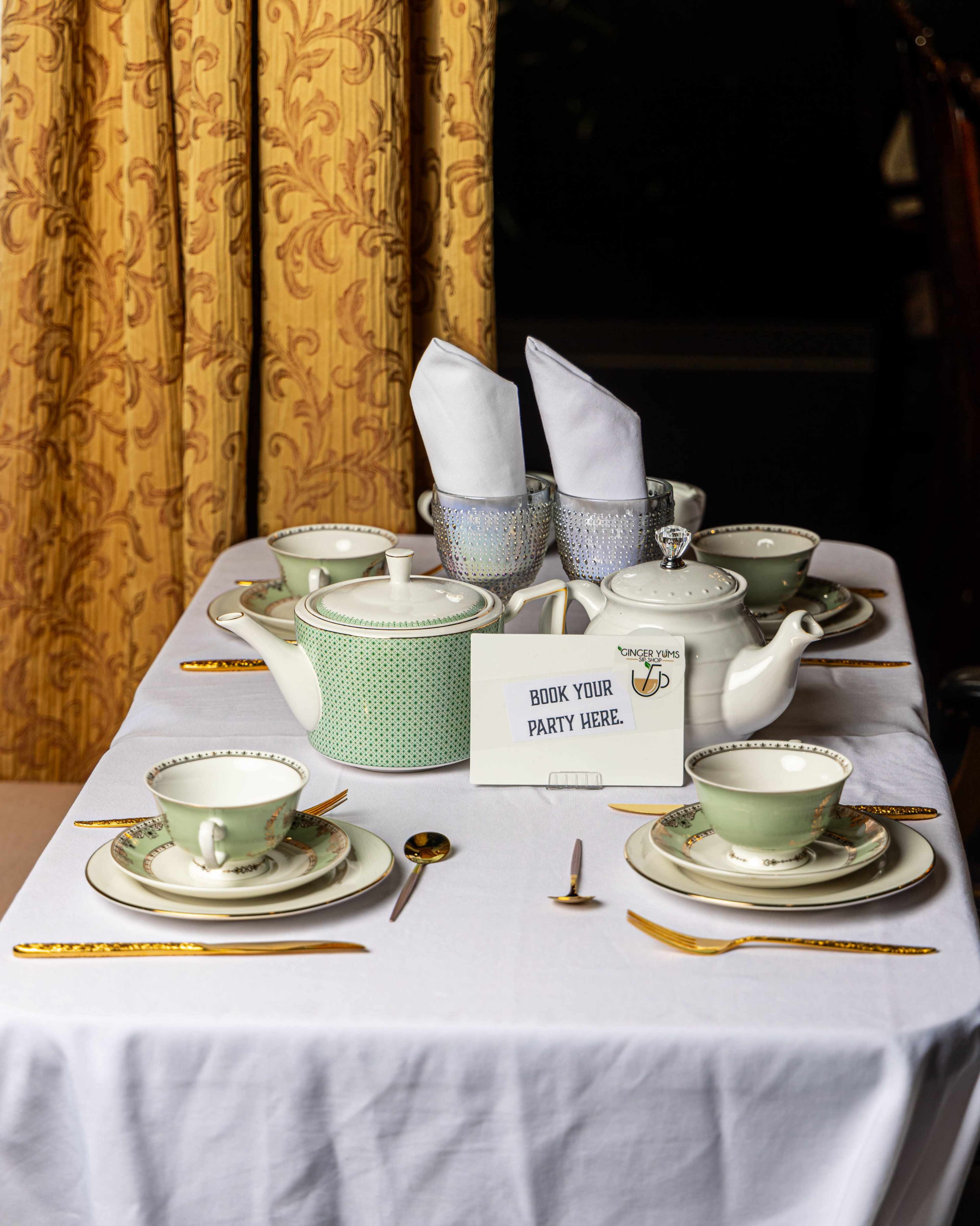 A neatly set dining table features elegant china, silverware, and a promotional sign for booking a party.