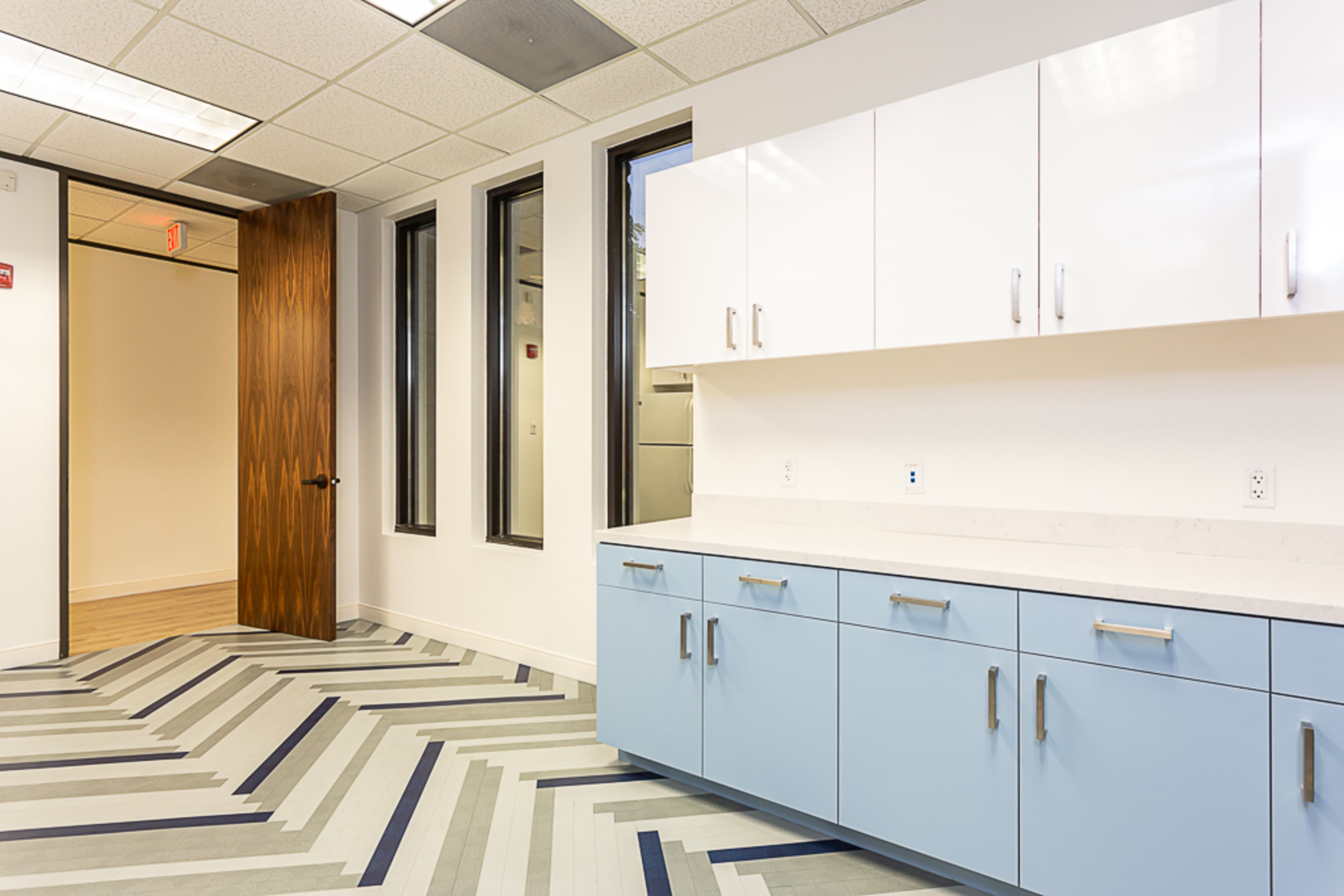 A modern office space with a blue and grey patterned floor, white cabinets, and a wooden door leading to another room.
