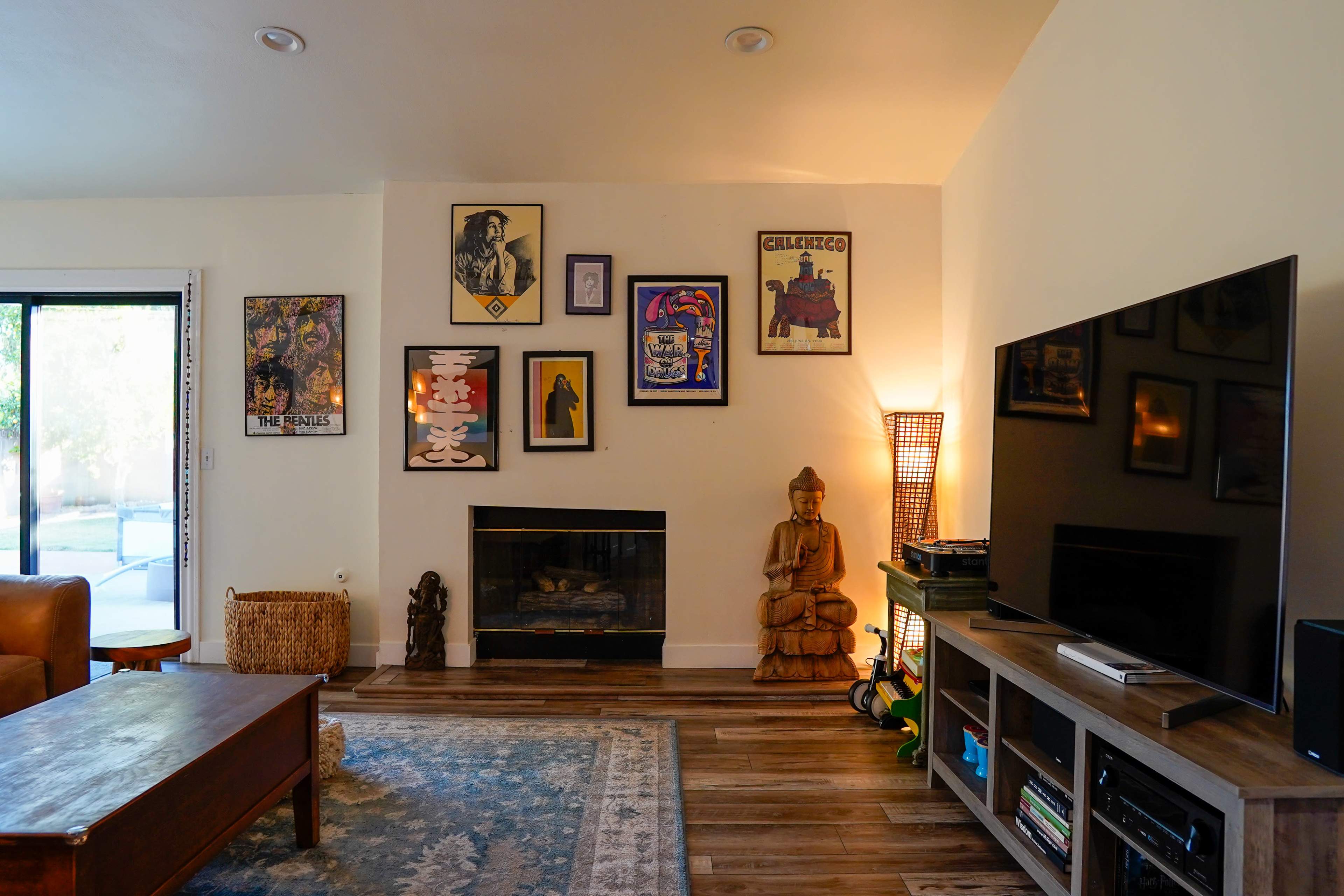 The living room features a television, a wooden coffee table, a fireplace surrounded by framed artwork, and a decorative Buddha statue beside a woven basket.