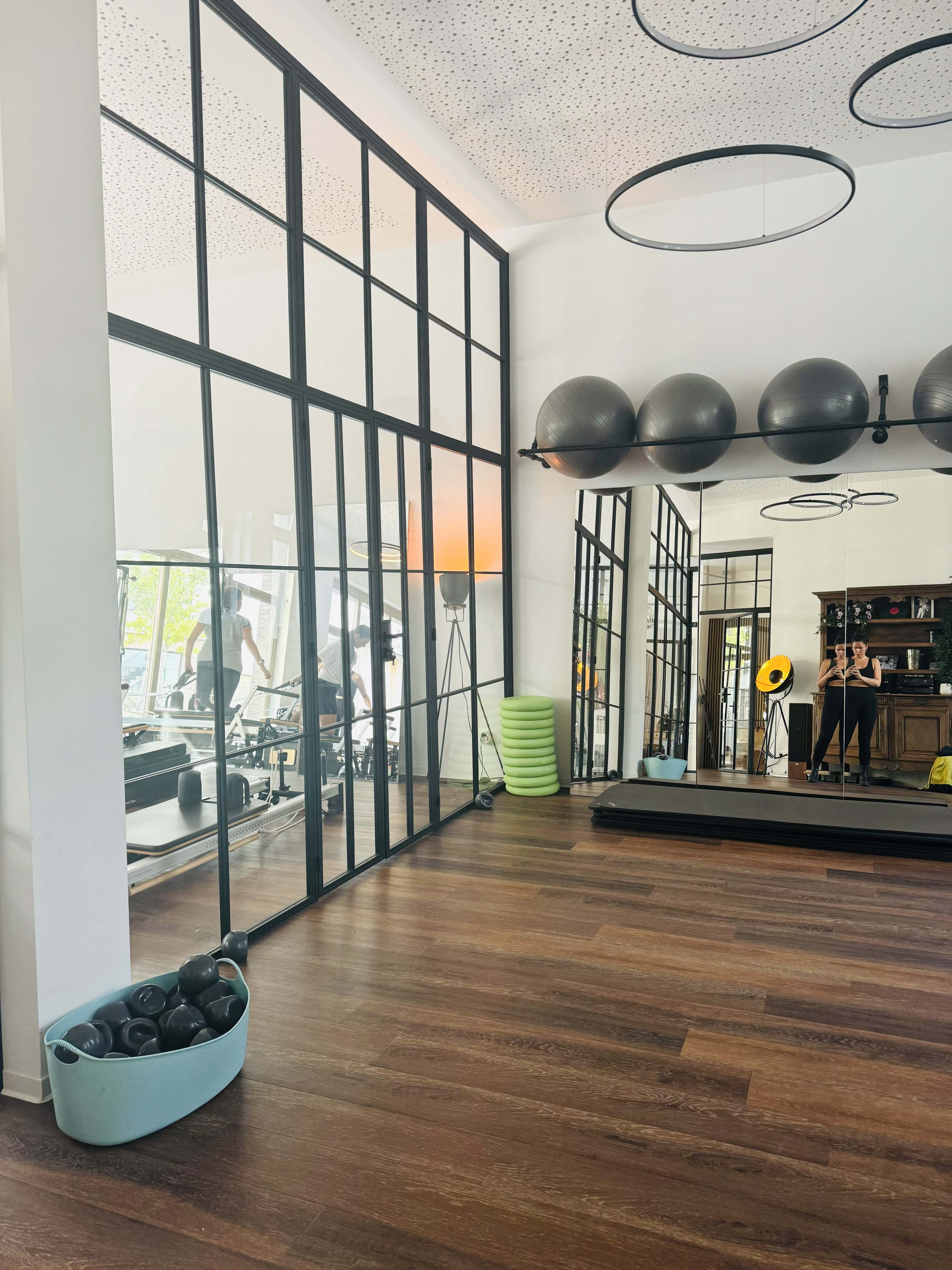 A fitness studio features large glass windows, exercise equipment, and a variety of workout balls arranged along the walls.