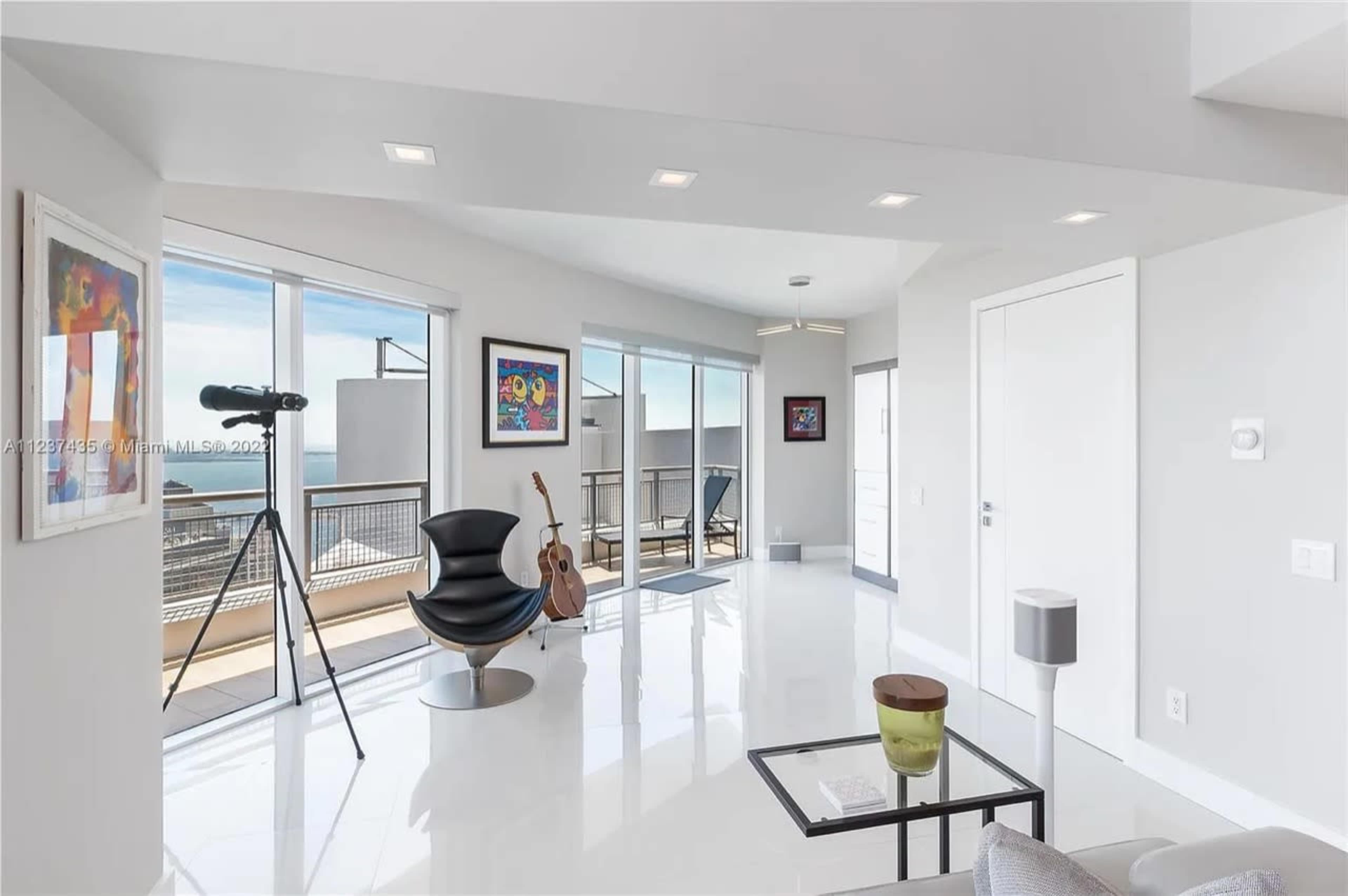 A modern living space features large windows, a telescope, a guitar, and minimalist furniture.