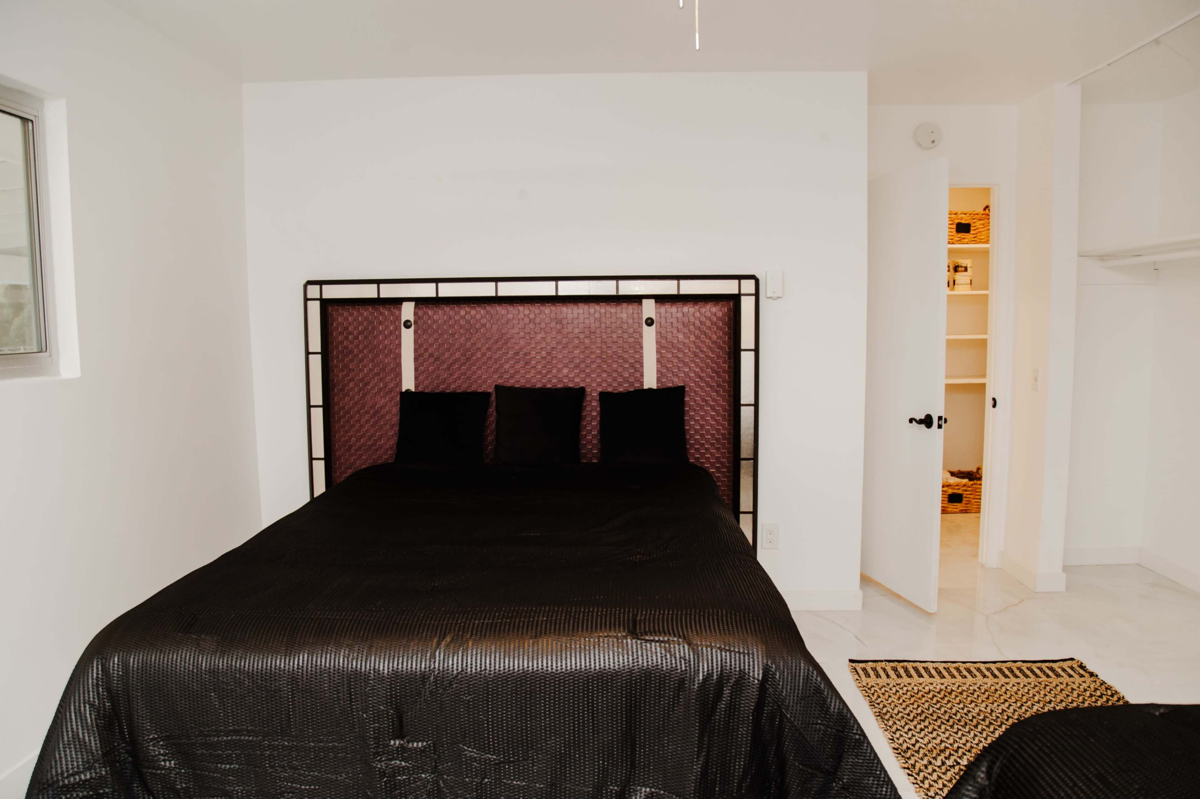 A bedroom featuring a black bedspread, a headboard with a burgundy panel, and a closet door partially open in the background.