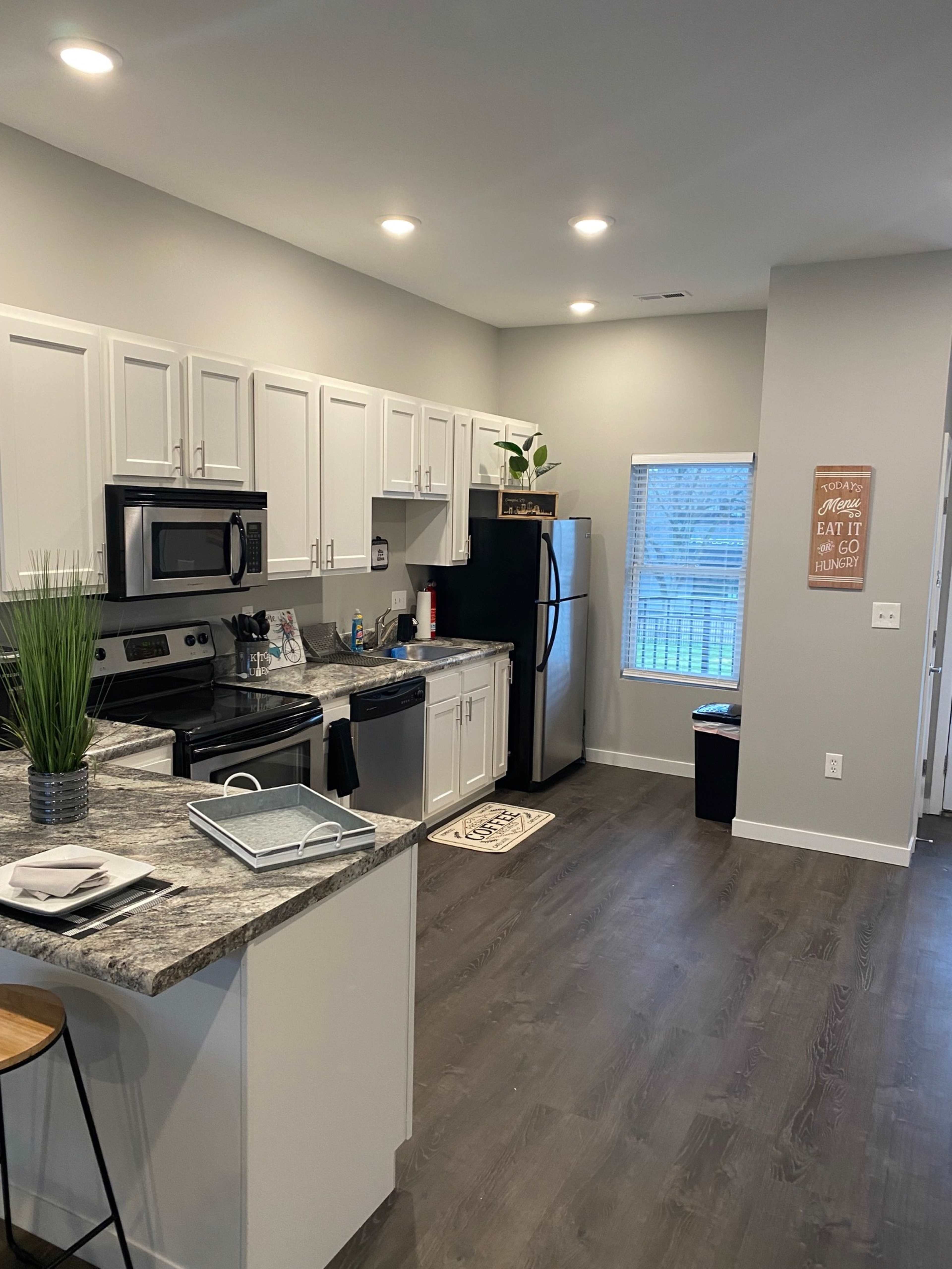 A modern kitchen with white cabinets, a stainless steel stove and microwave, and a granite countertop, featuring a window that provides natural light.