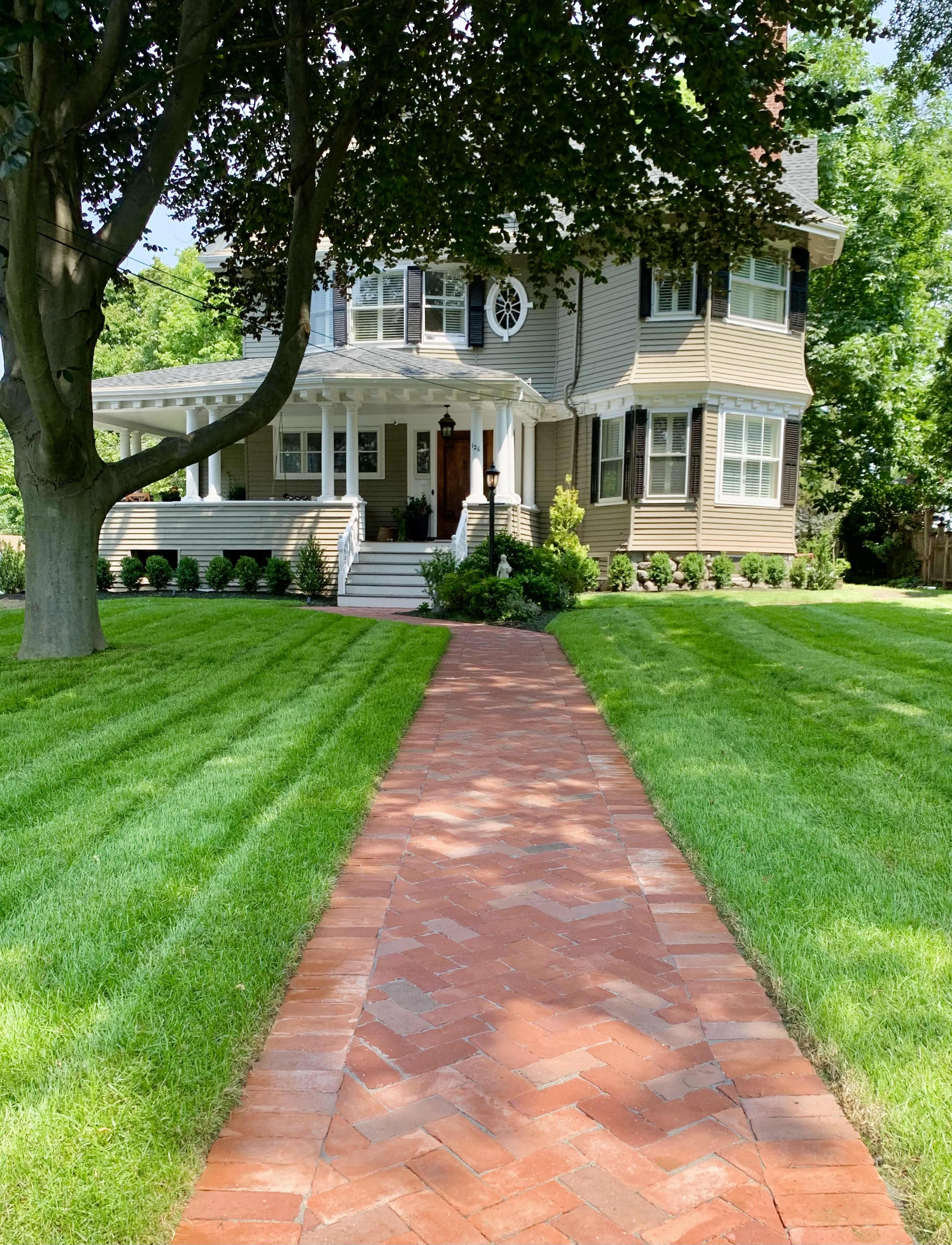 A brick walkway leads to a large, two-story house surrounded by well-maintained grass and landscaped gardens.
