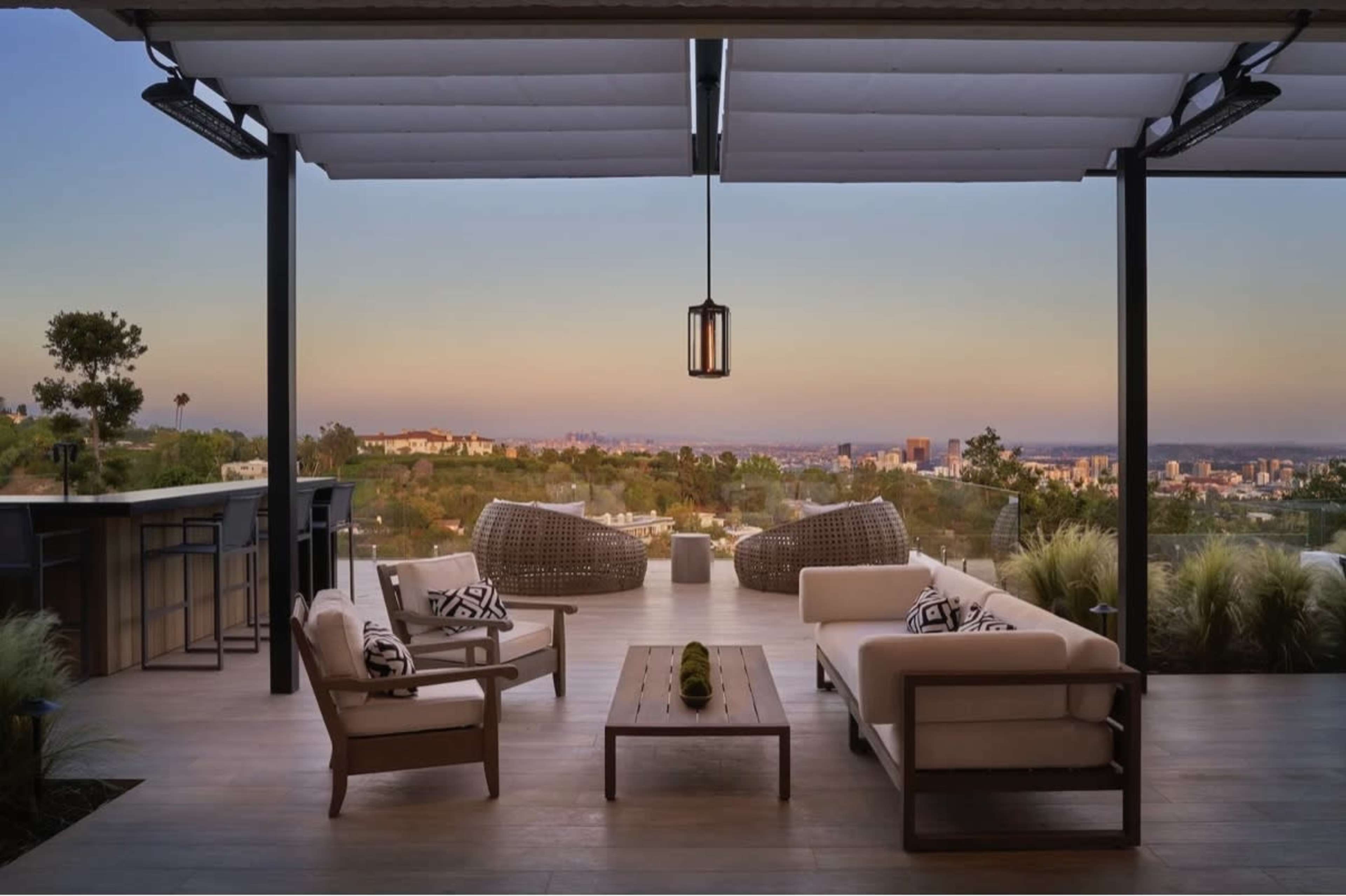 A modern outdoor patio features comfortable seating, a wooden table, and a panoramic view of the city skyline at dusk.