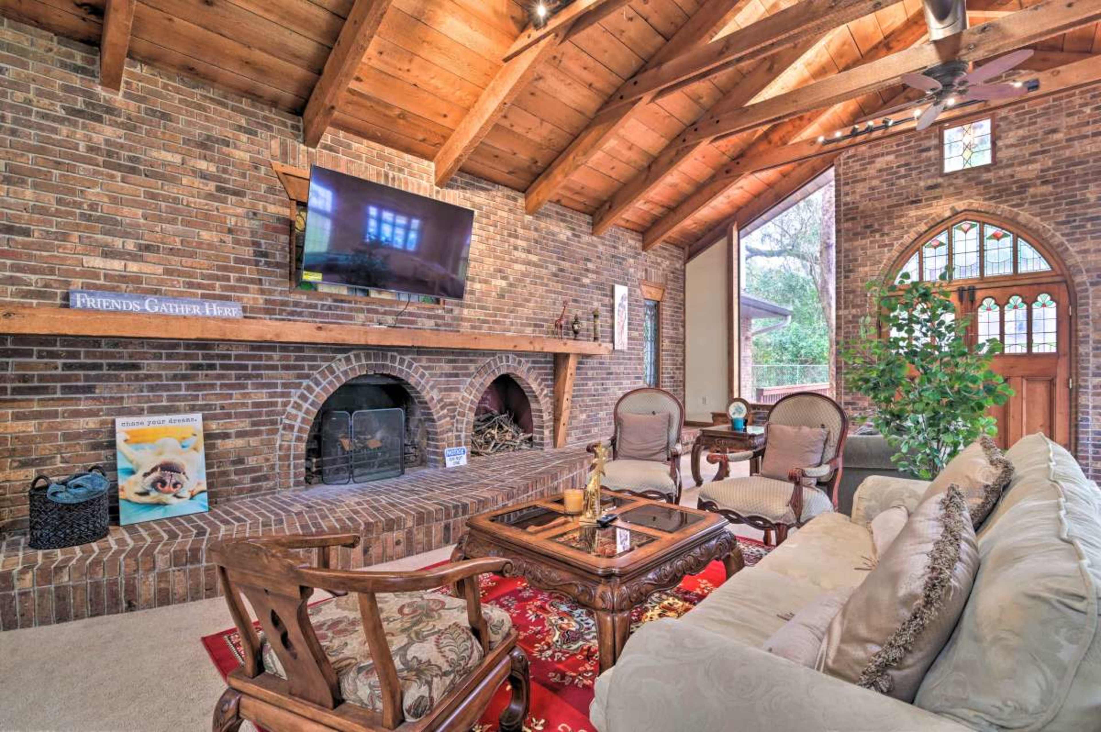 A living room with a brick wall, wooden ceiling beams, a fireplace, and comfortable seating arrangements.