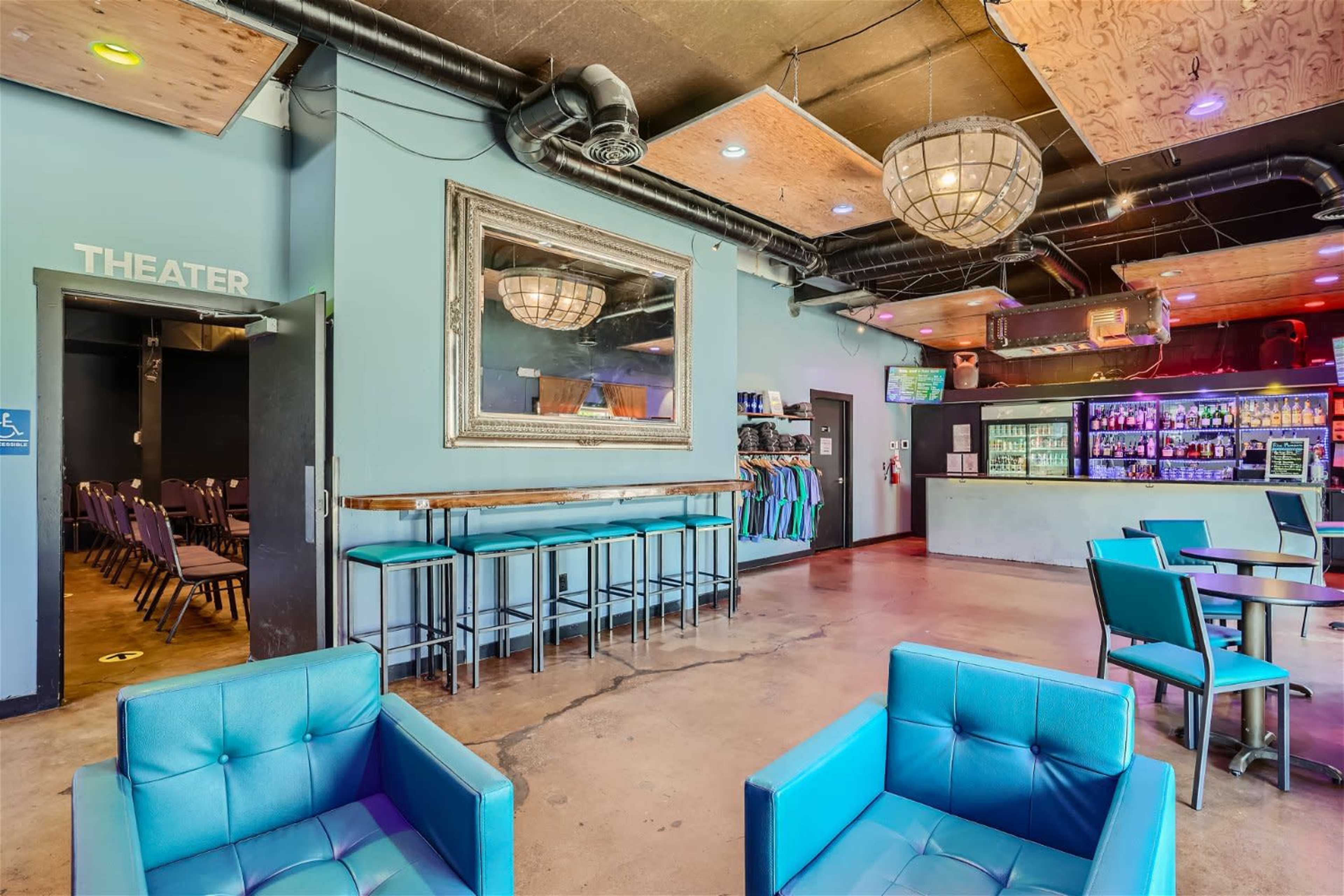A modern lounge area with turquoise chairs, a bar with various drinks, and a theater entrance marked on the wall.