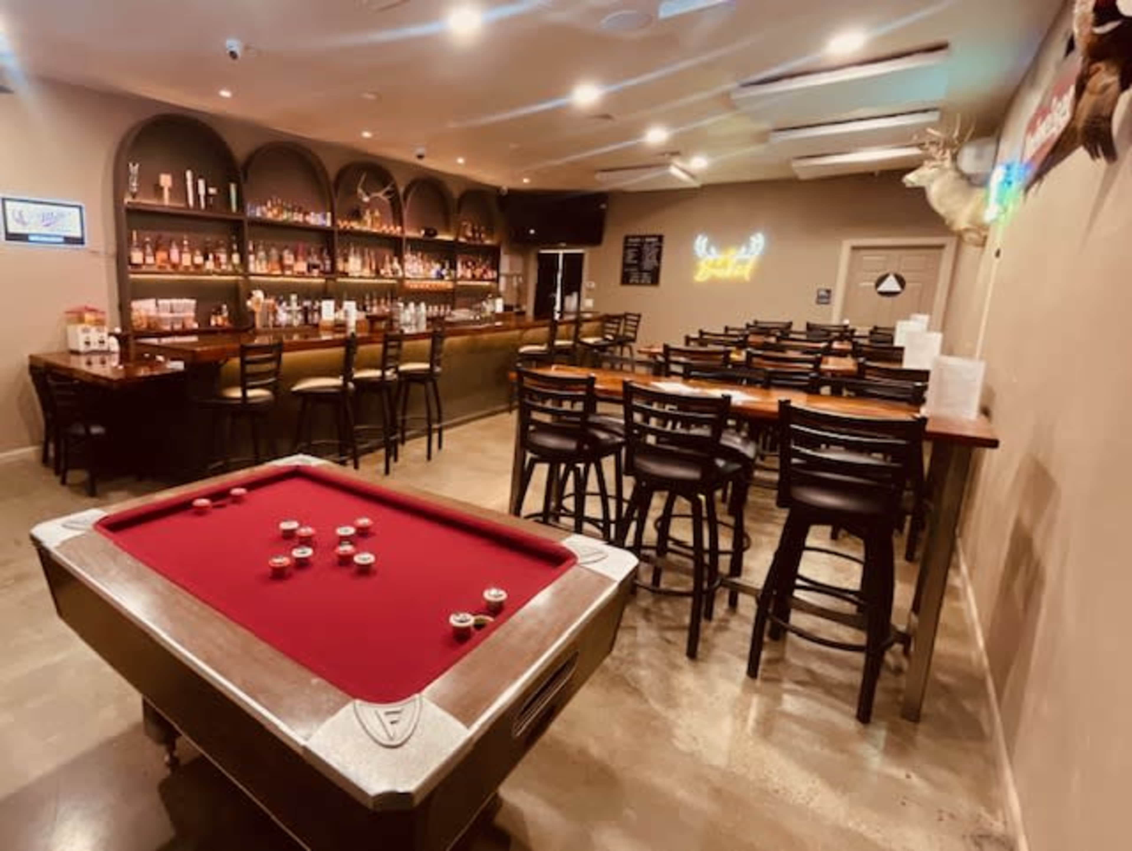 The image shows a bar area with a pool table in the foreground, surrounded by bar stools and a well-stocked back bar.