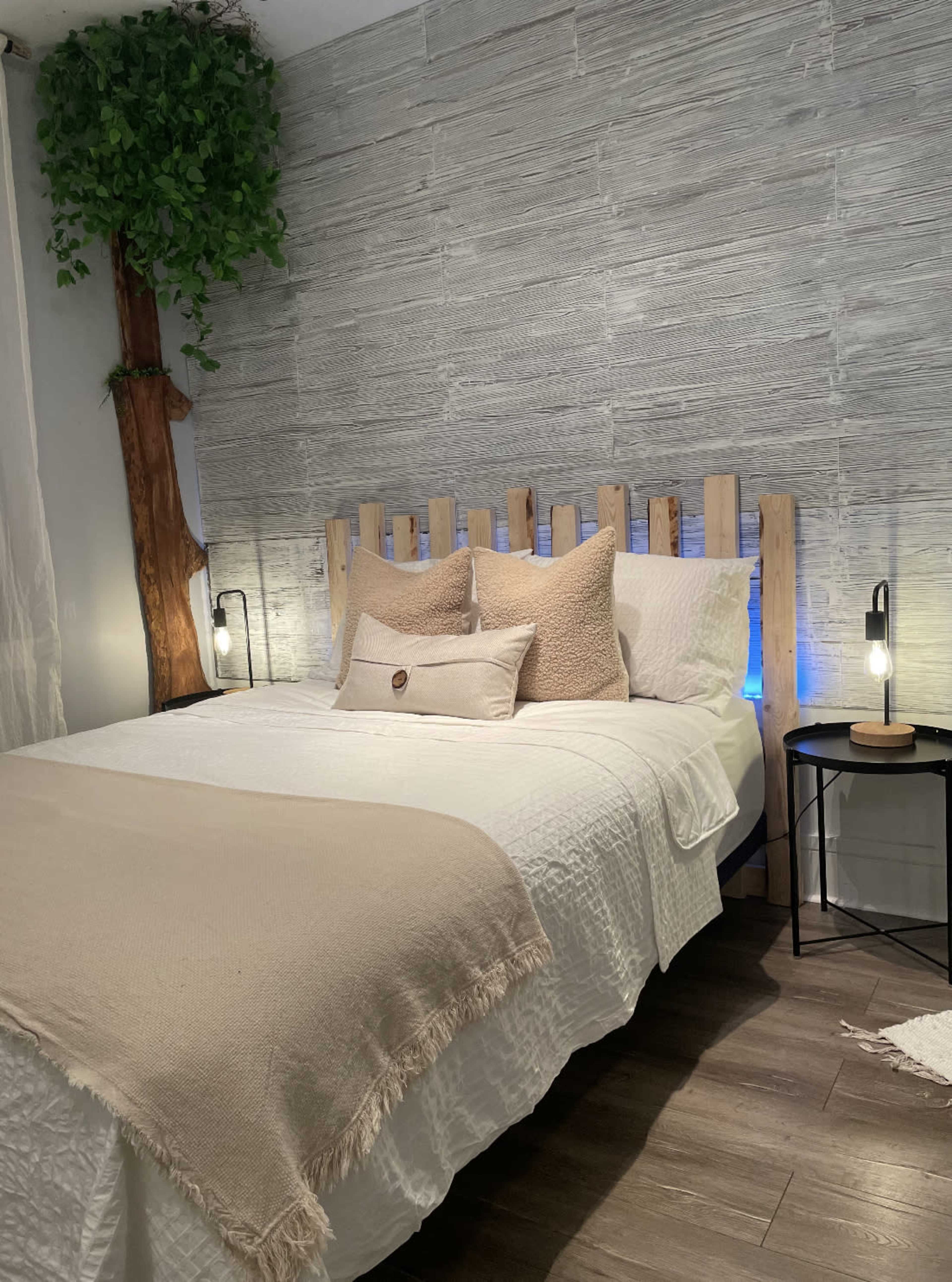 A neatly made bed with a wooden headboard and decorative pillows is positioned against a textured wall, accompanied by bedside lamps and a small table.