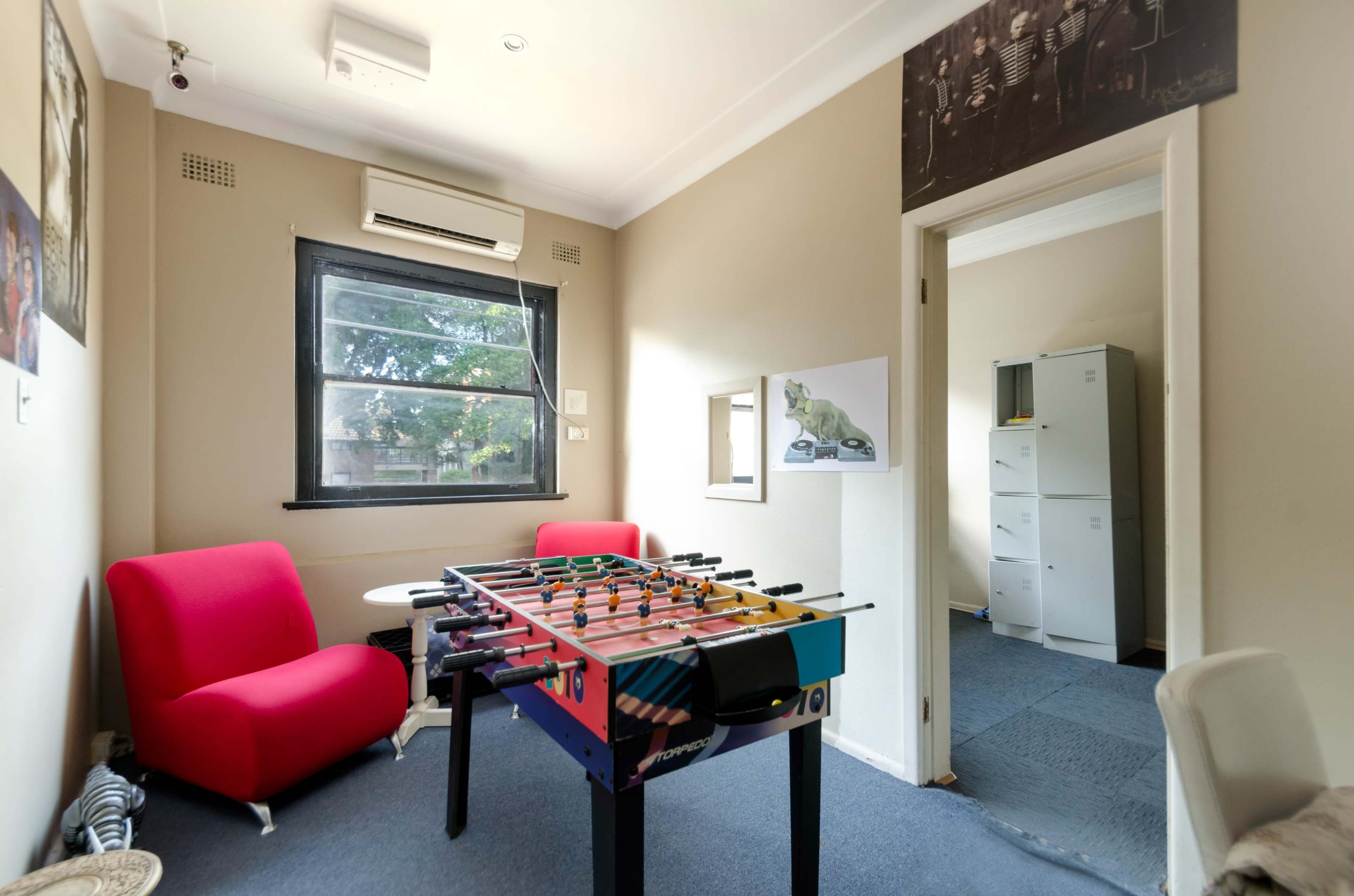 A small, tidy room with a foosball table, a red couch, and an open doorway leading to another room featuring filing cabinets.