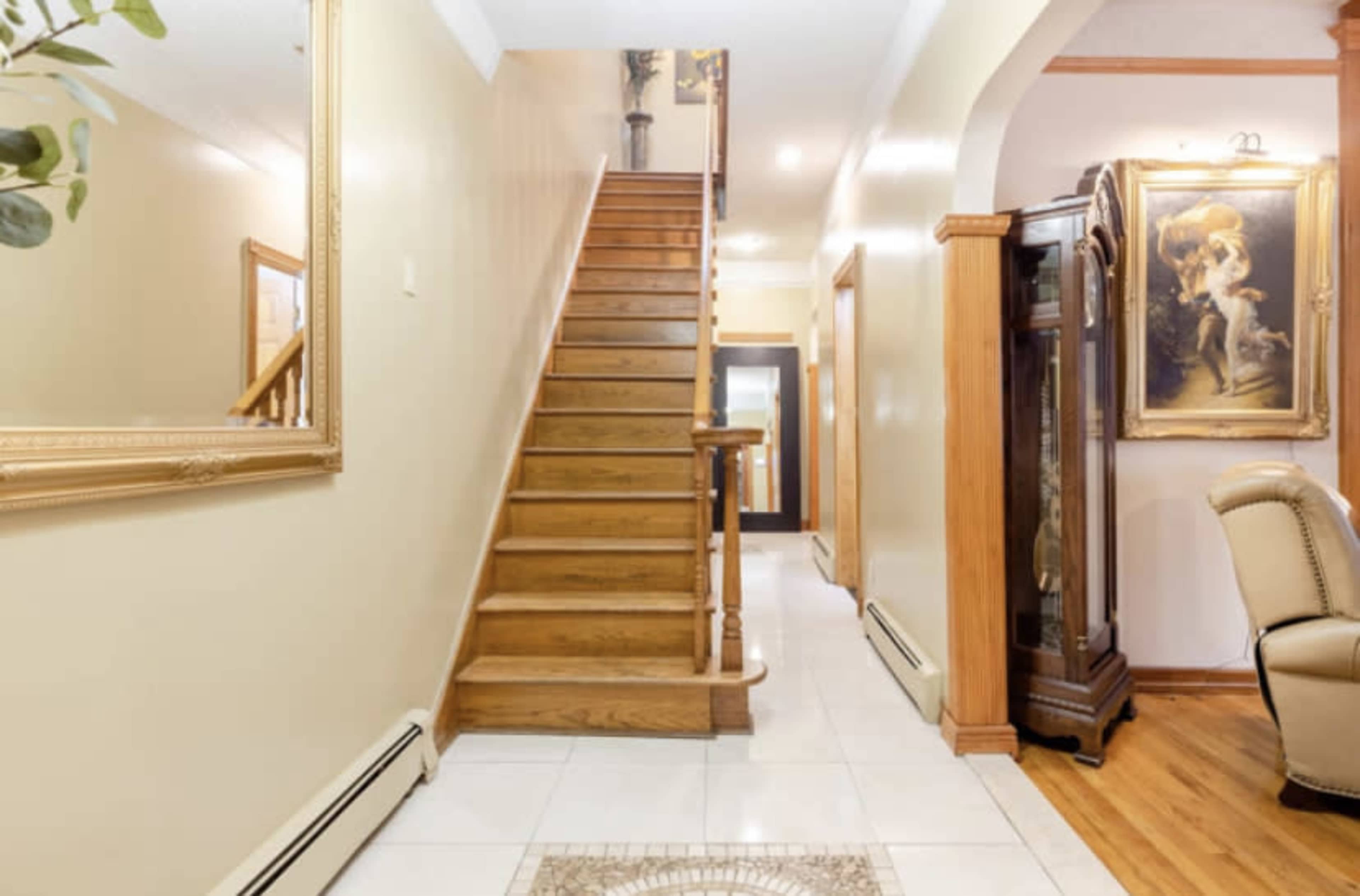 A well-lit hallway features a staircase leading to an upper level, with a mirror and a decorative cabinet on either side.