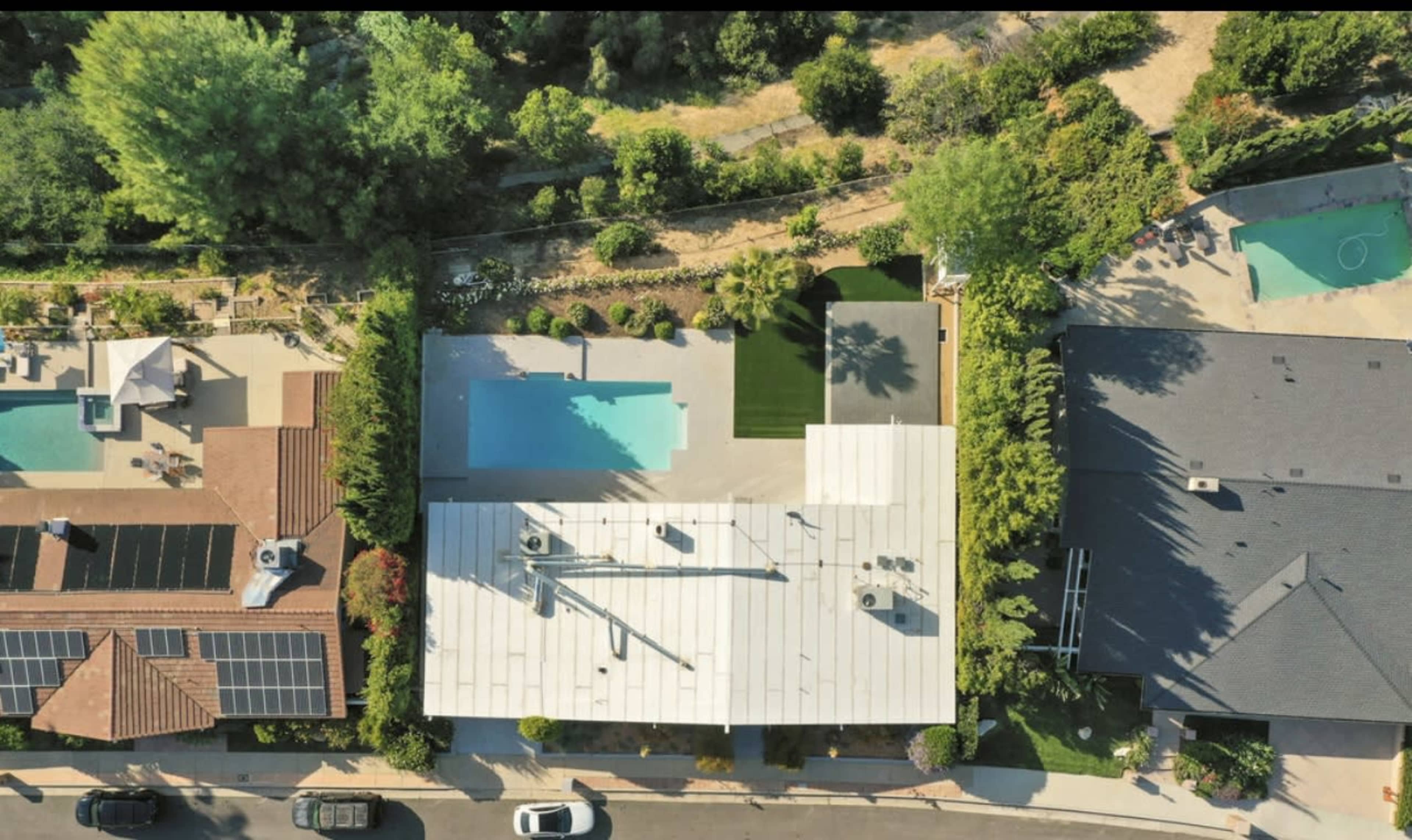 An aerial view shows two houses with swimming pools and landscaped yards in a suburban neighborhood.