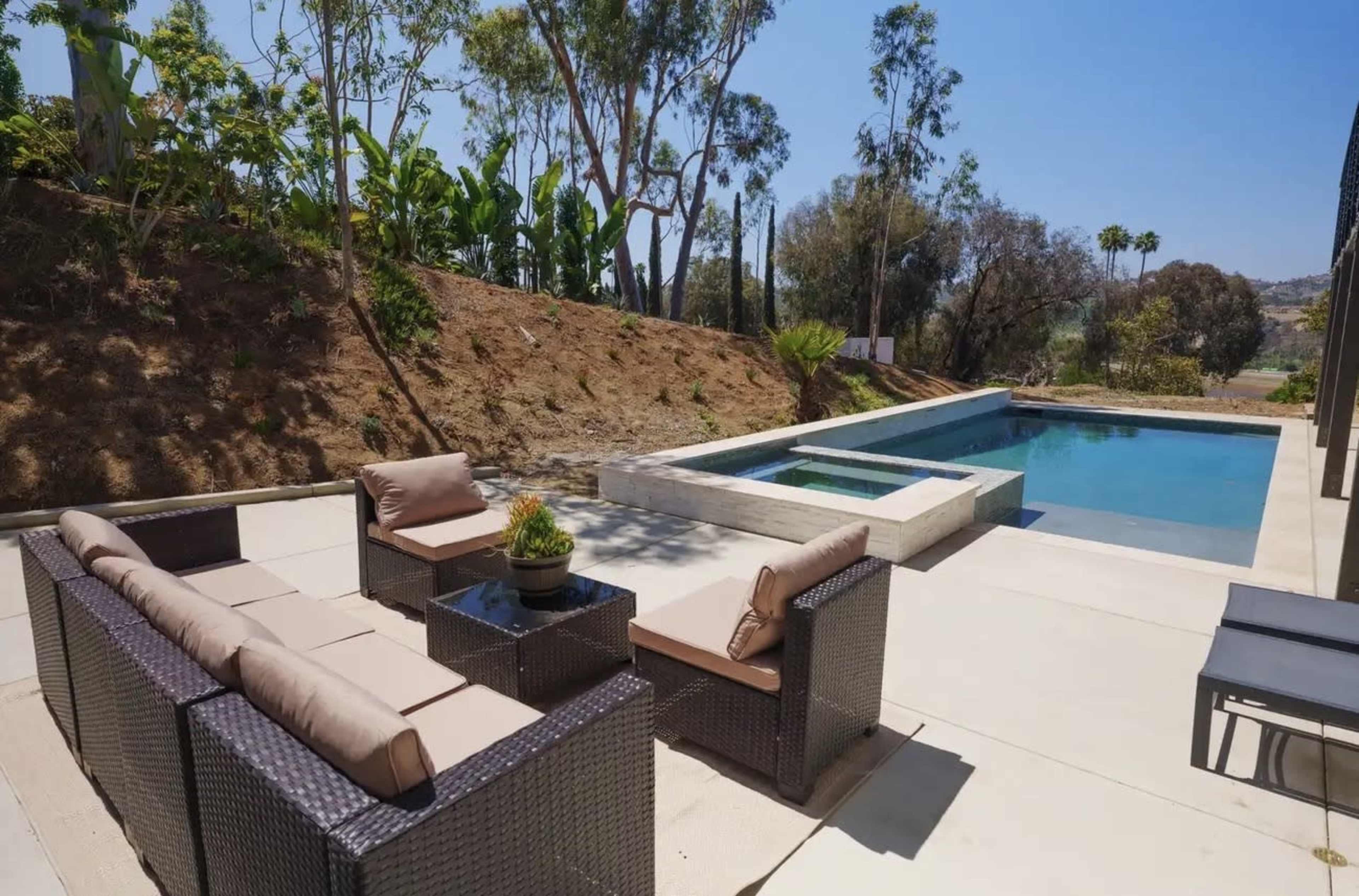 The image features a patio area with outdoor seating and a swimming pool surrounded by landscaping.