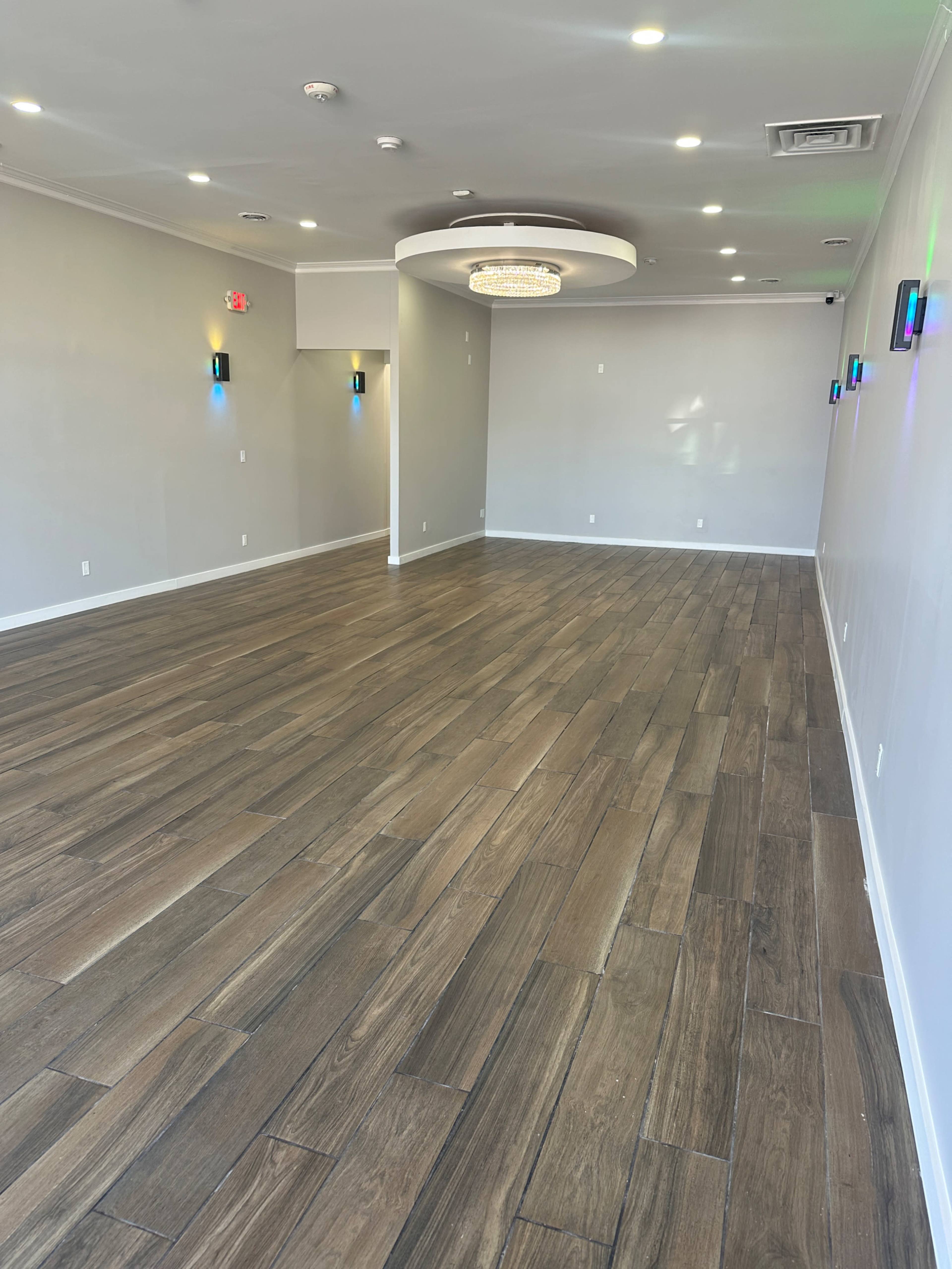 The image shows a spacious, well-lit interior with wooden flooring and modern lighting fixtures on the ceiling.