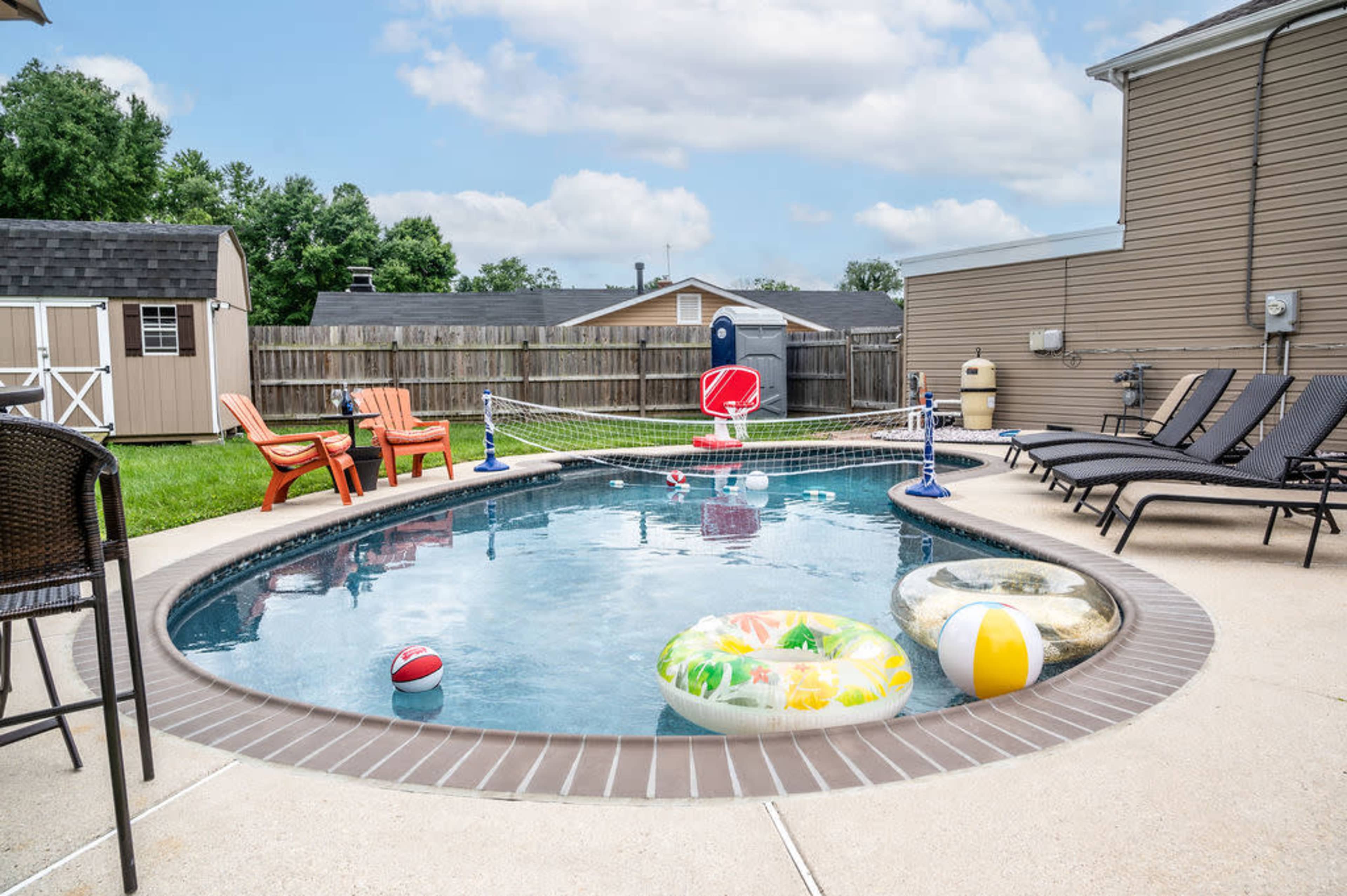A backyard swimming pool surrounded by lounge chairs and colorful pool floats on a sunny day.