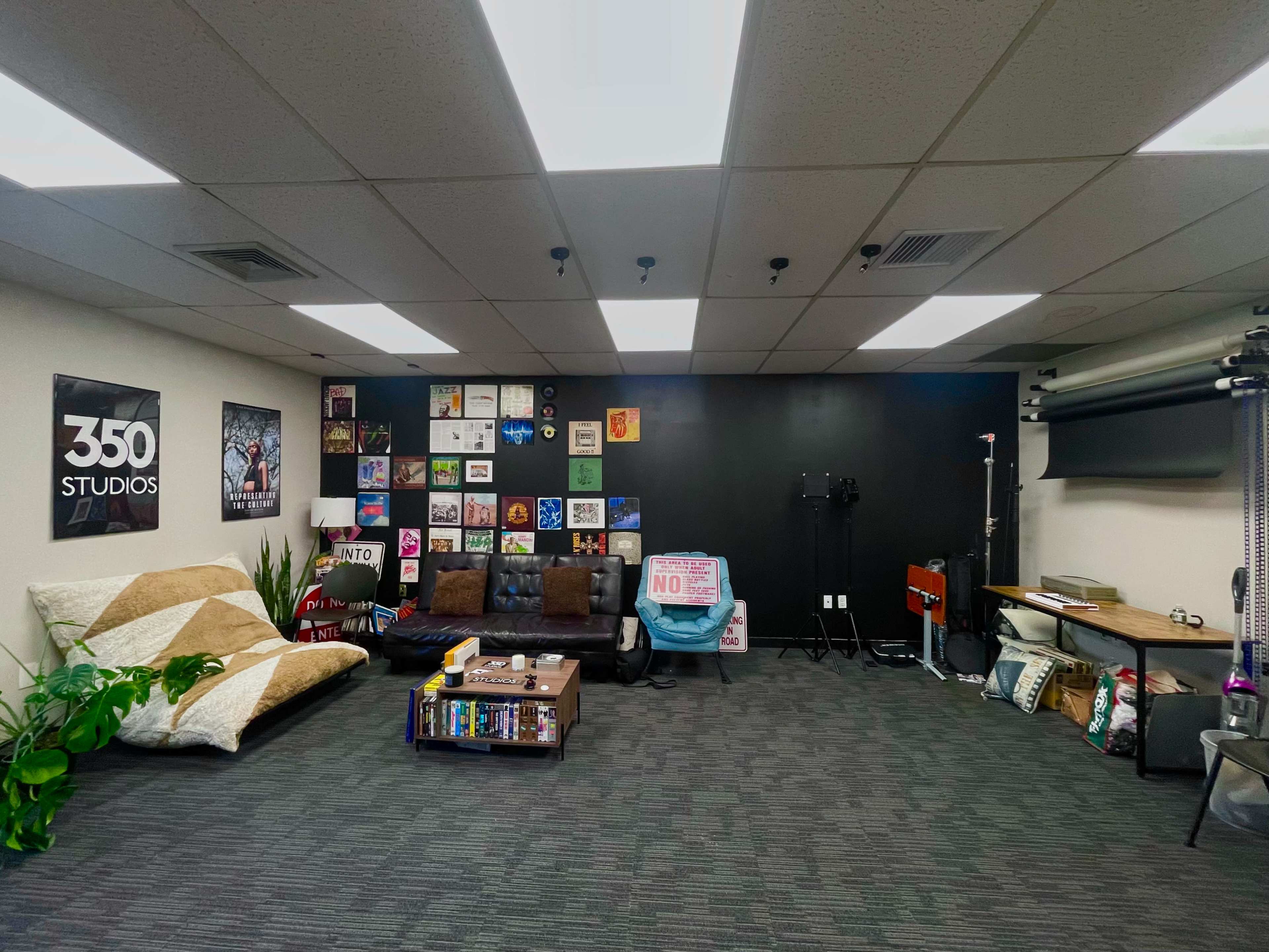 A studio space with a dark accent wall adorned with various framed art pieces, a brown couch, a patterned rug, and several studio equipment items arranged along the sides.