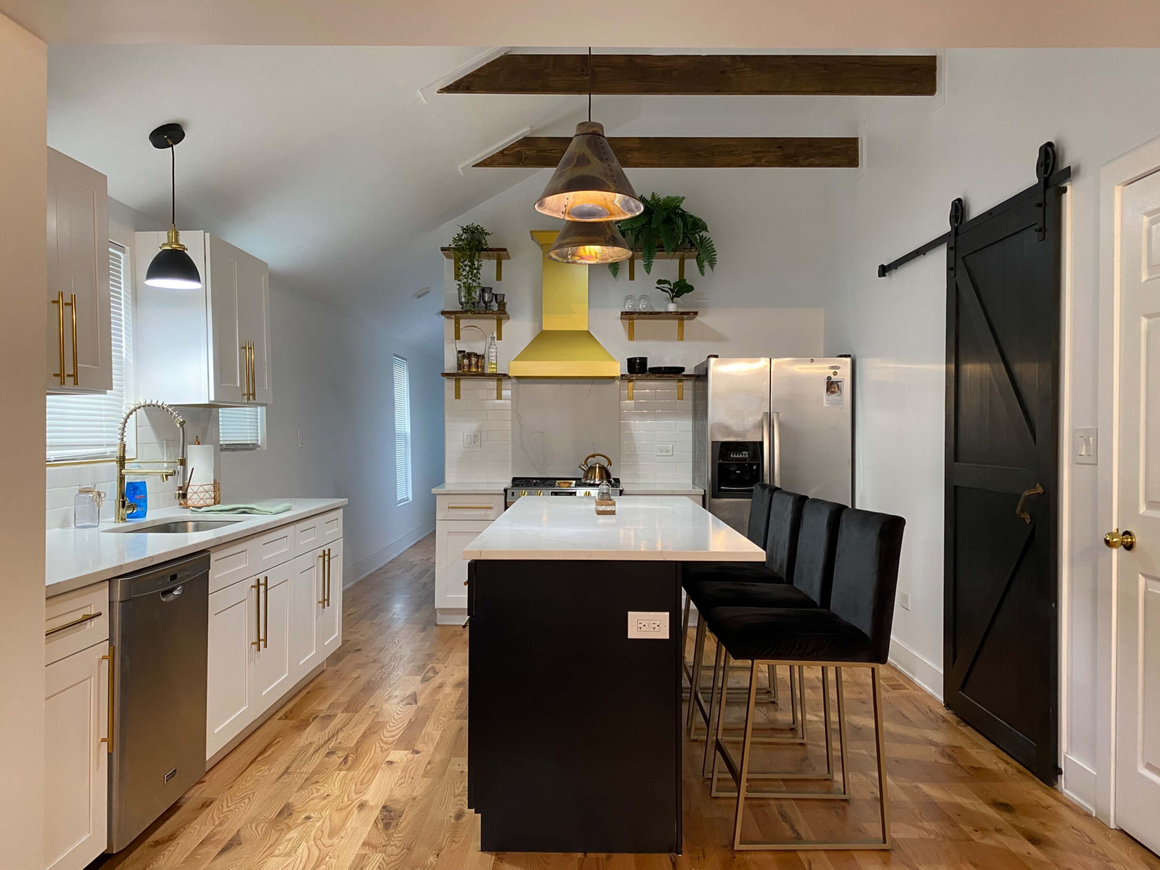 A modern kitchen features white cabinetry, a central island with bar stools, and a yellow range hood above the stove.
