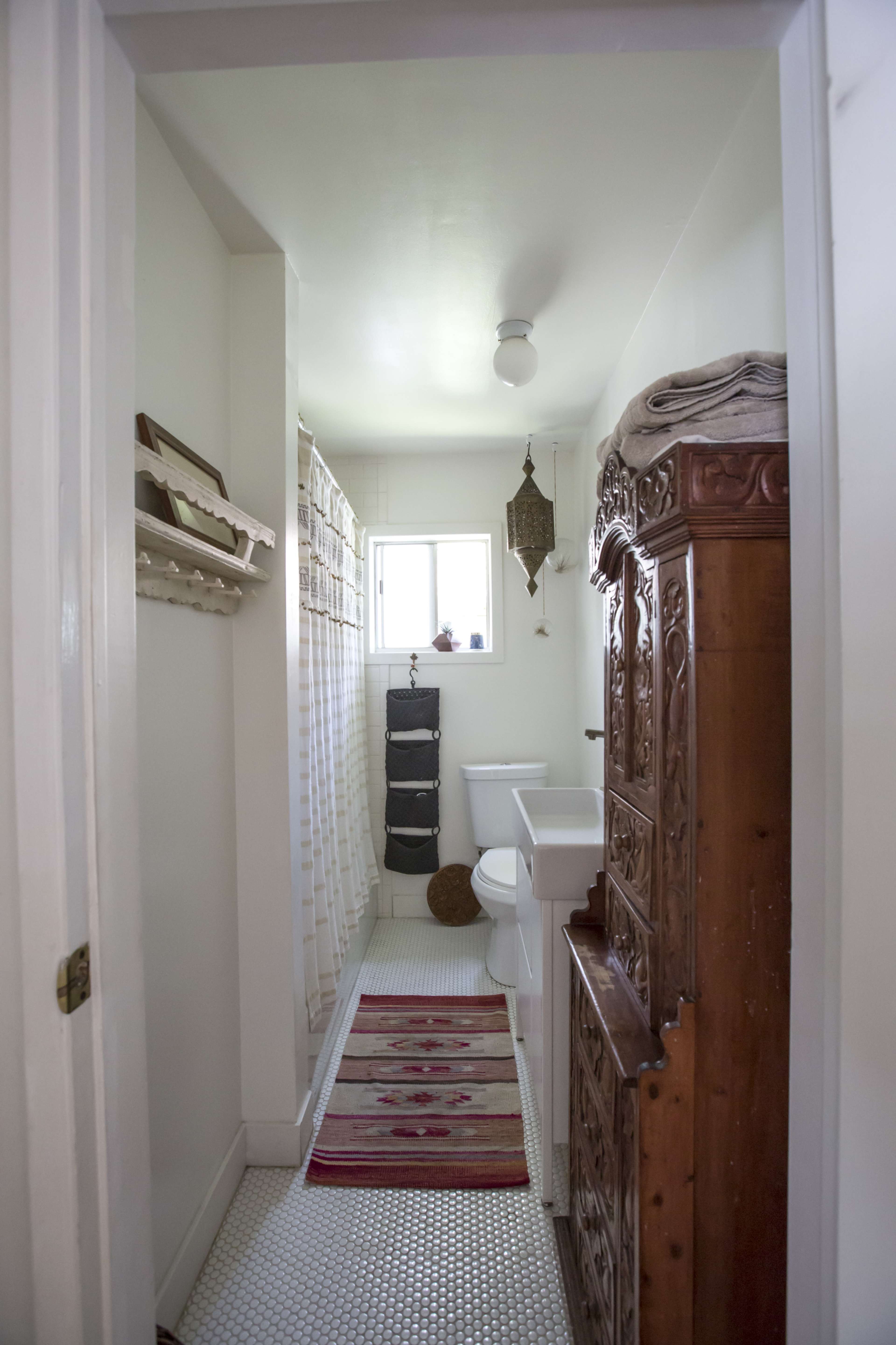 A narrow bathroom with a shower curtain, a toilet, a sink, and a decorative wooden cabinet along one wall.