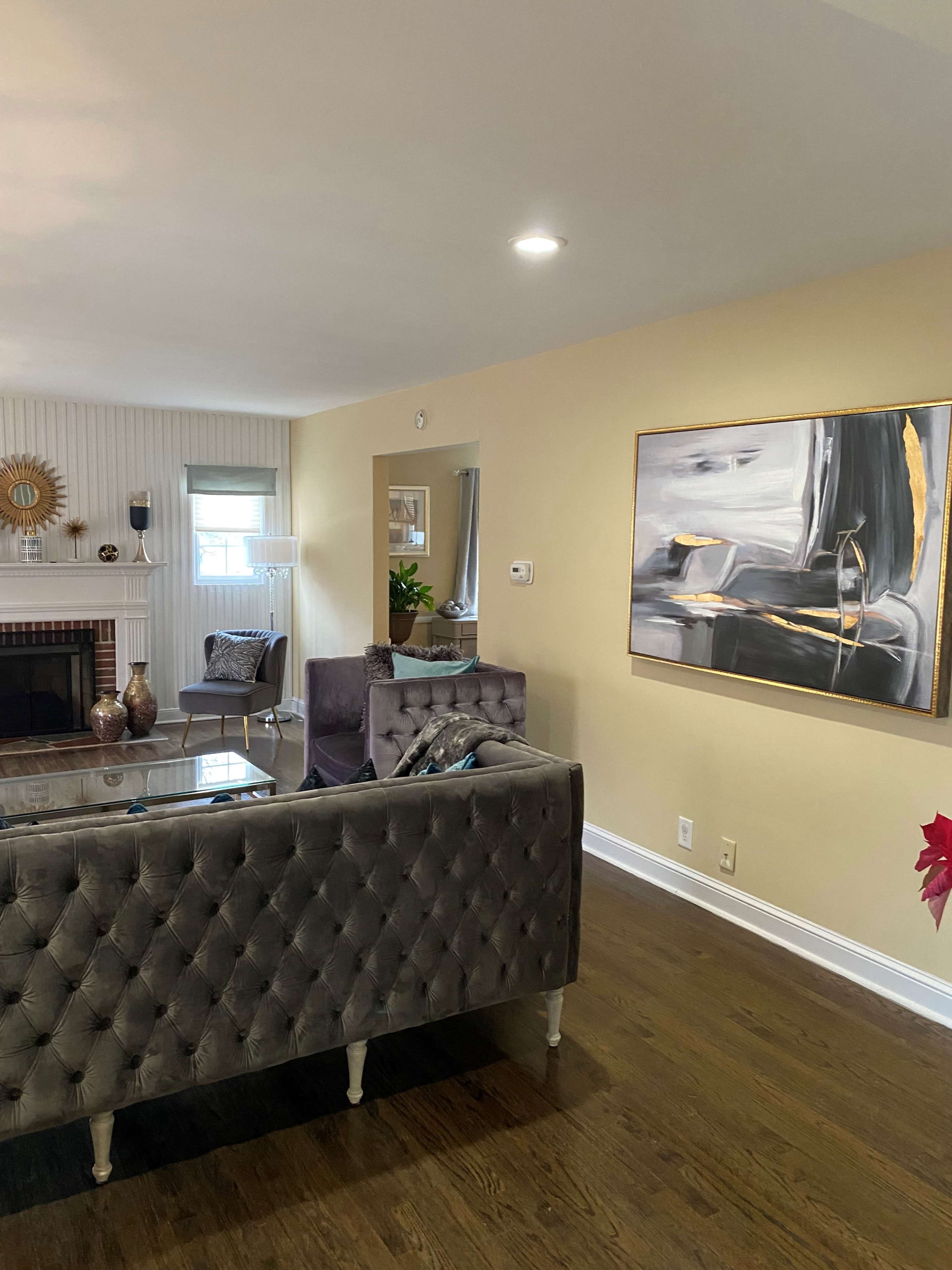 A living room with a gray tufted sofa, a glass coffee table, and an abstract painting on the wall.