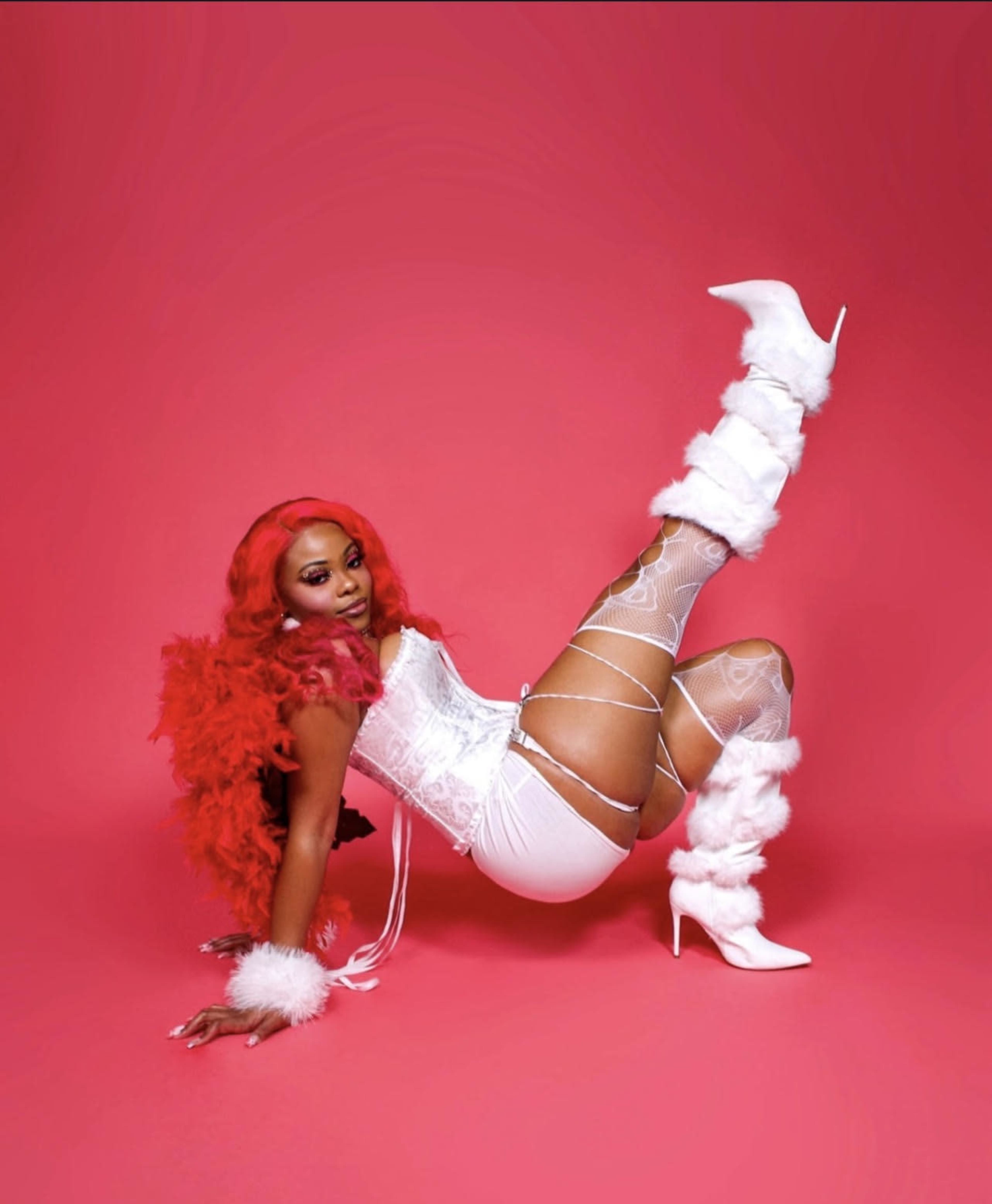 A person poses on a pink background, wearing a white outfit with fur accents and high heels.